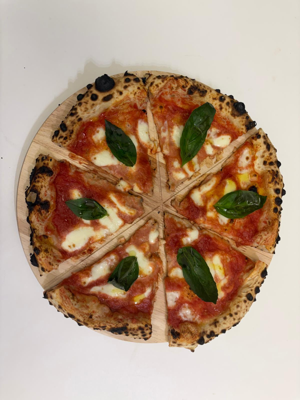 Pizza tagliata in sei fette, condita con salsa di pomodoro, mozzarella e basilico, su un tagliere di legno.