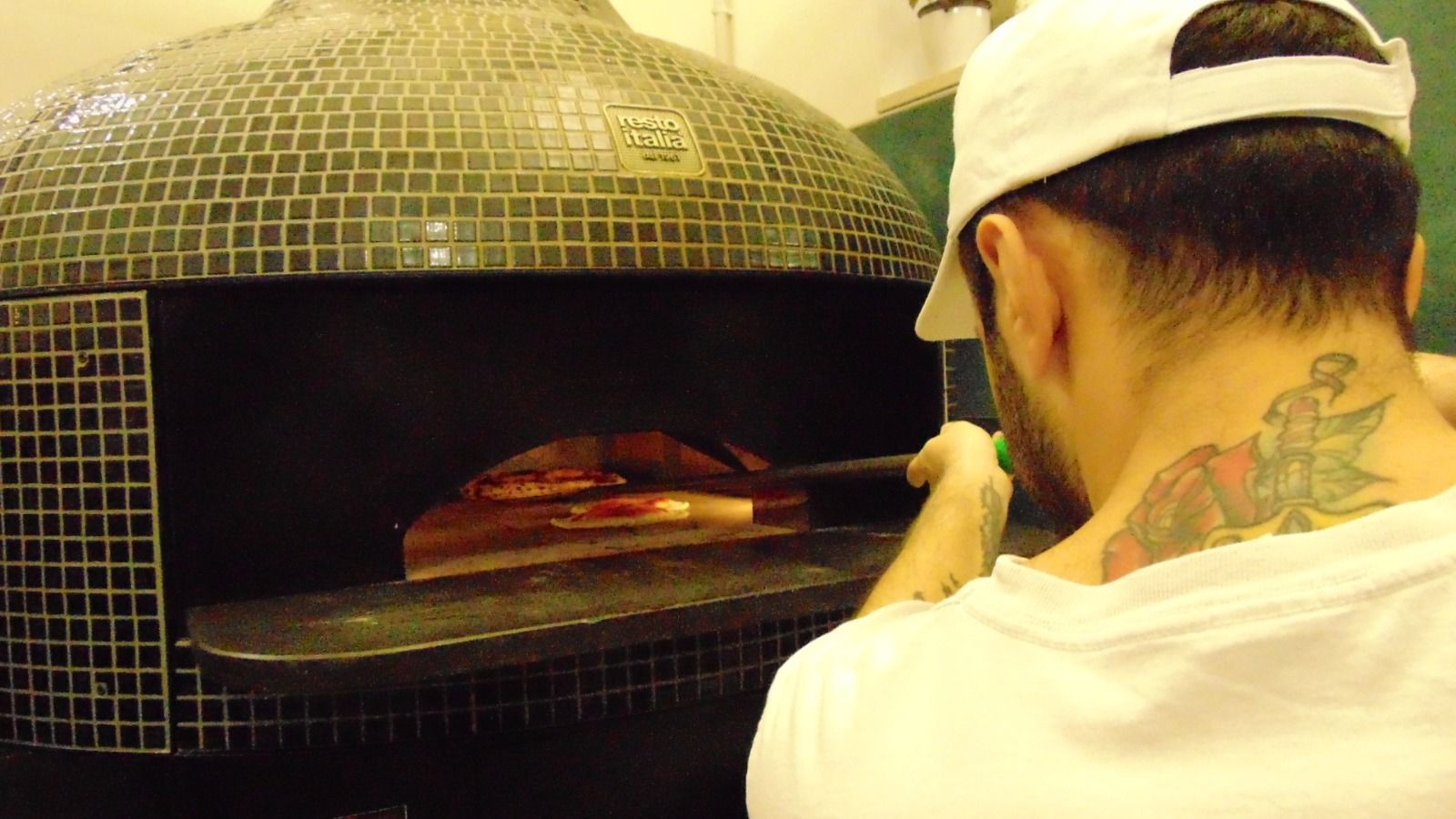 Uomo con tatuaggio sul collo che mette la pizza nel forno a legna.