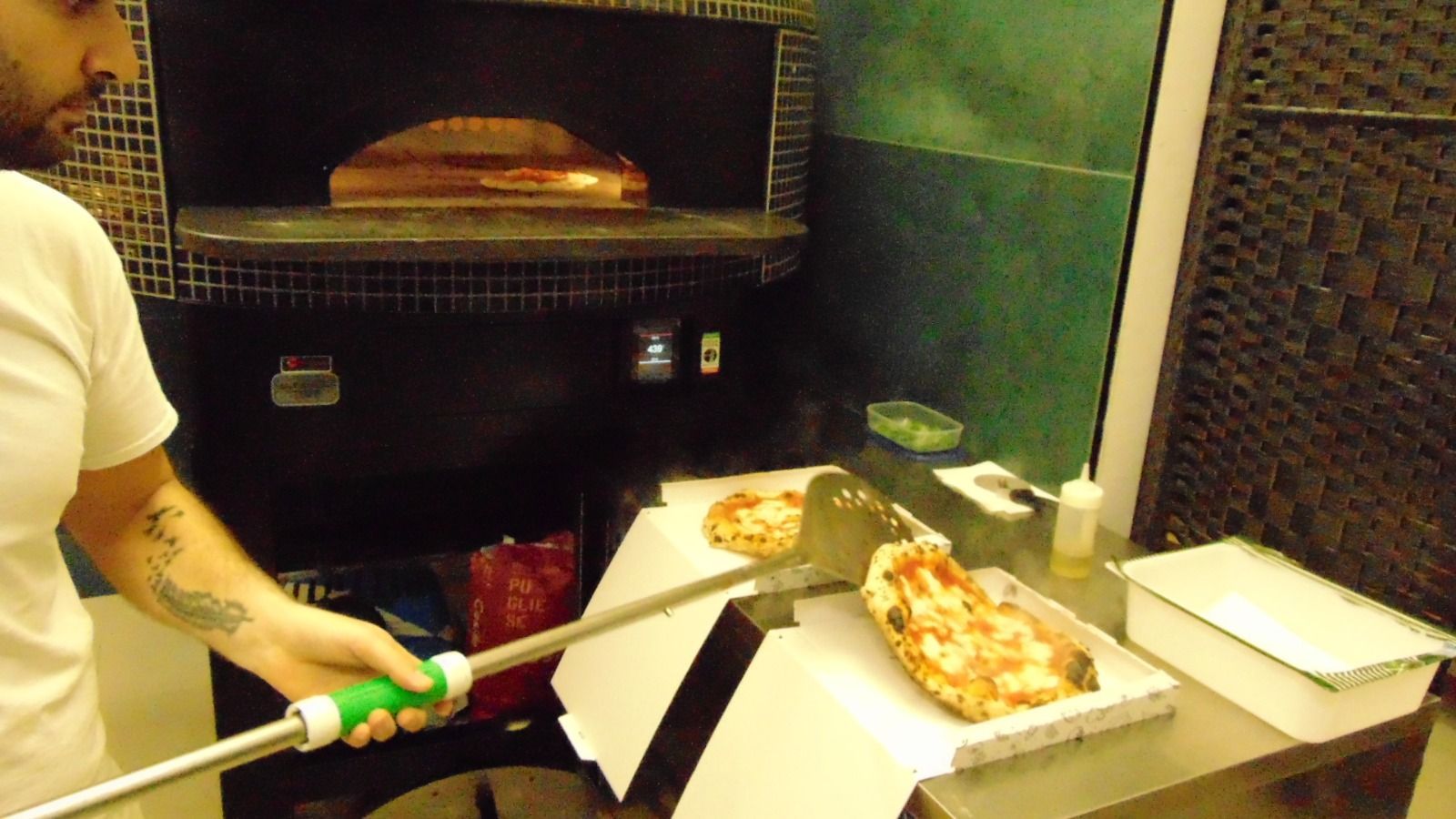 Chef che estrae la pizza dal forno a legna con una pala. Ambiente di cucina professionale al chiuso.