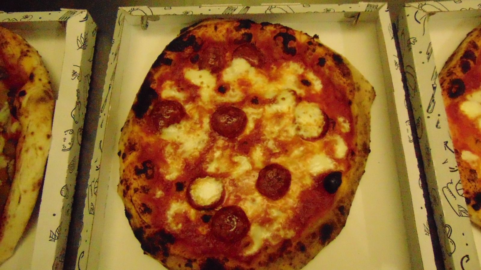 Pizza in scatola di cartone, con salame piccante e formaggio bianco, crosta leggermente bruciacchiata.