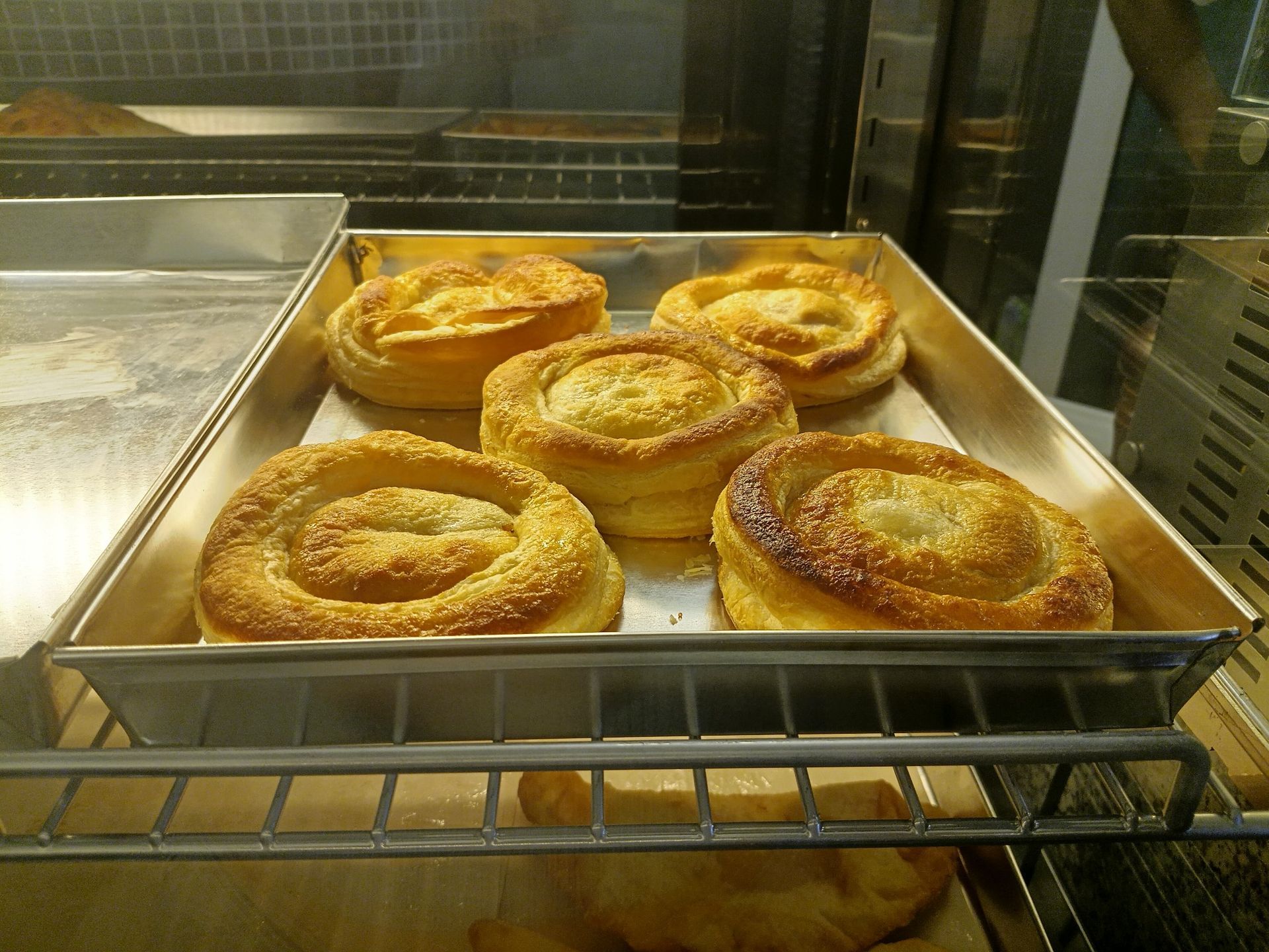 Pasticcini cotti al forno in una teglia di metallo dietro un vetro. Sono dorati e hanno un design a spirale.