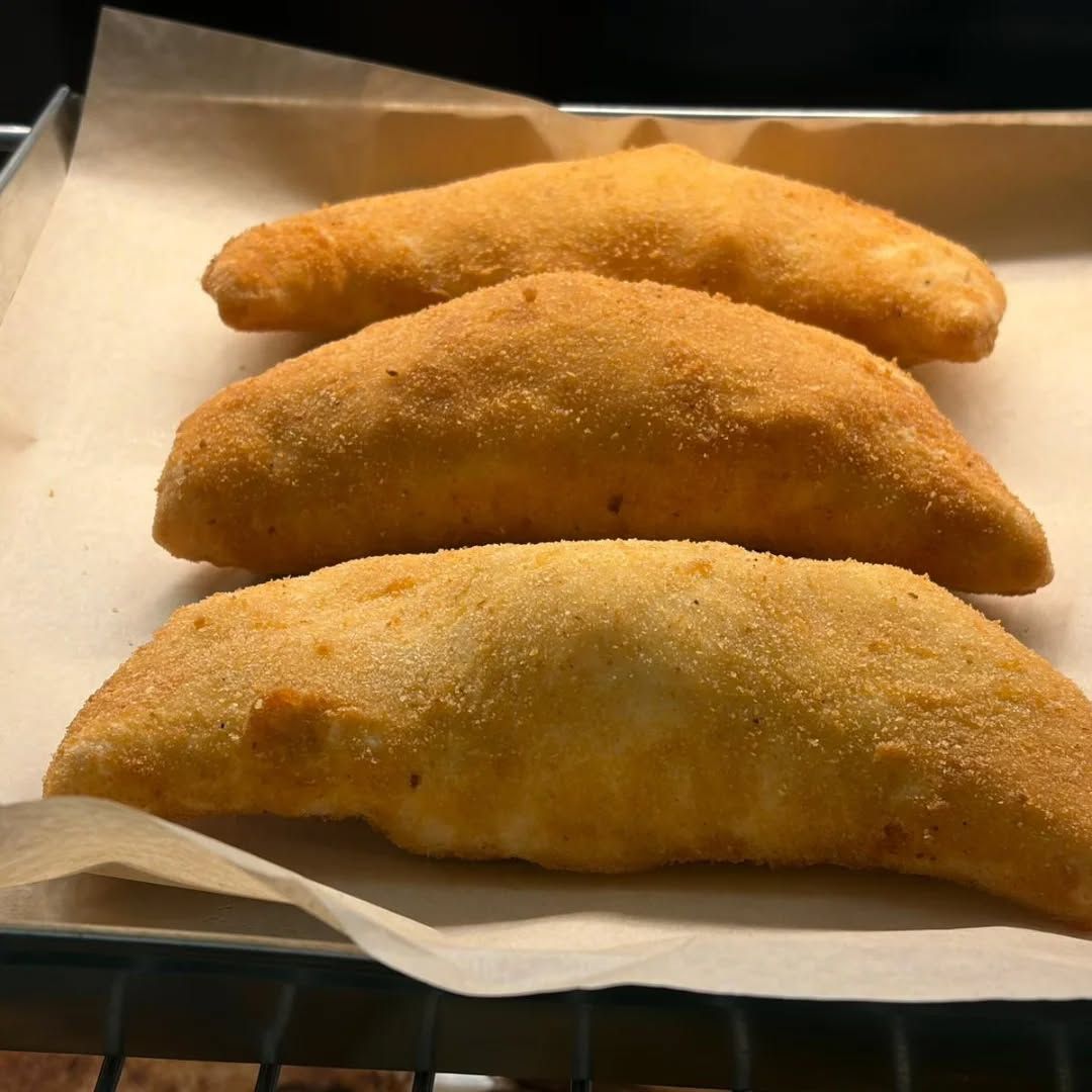 Tre calzoni dorati su carta da forno in un vassoio di metallo.