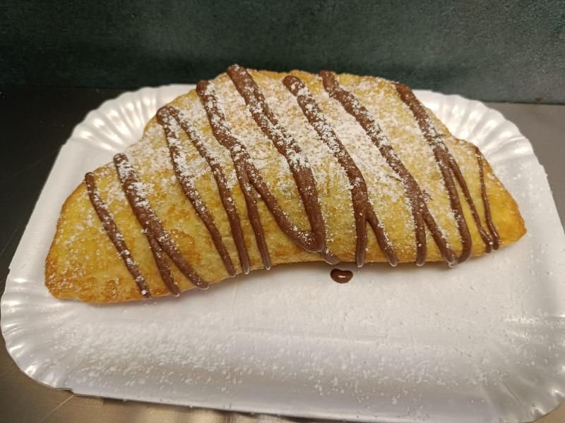 Pasta fritta ricoperta di cioccolato e spolverata di zucchero a velo, su un piatto di carta bianco.
