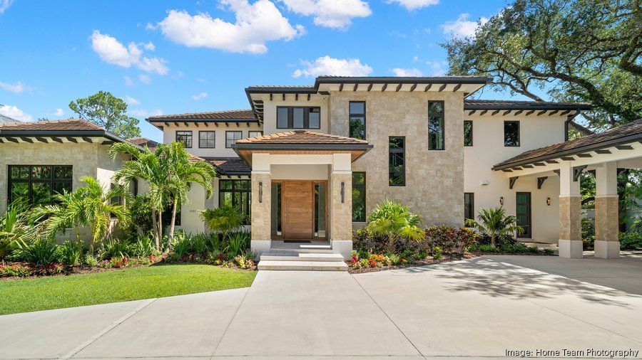 Modern two-story stone house with a front entry, driveway, and landscaped yard under a blue sky