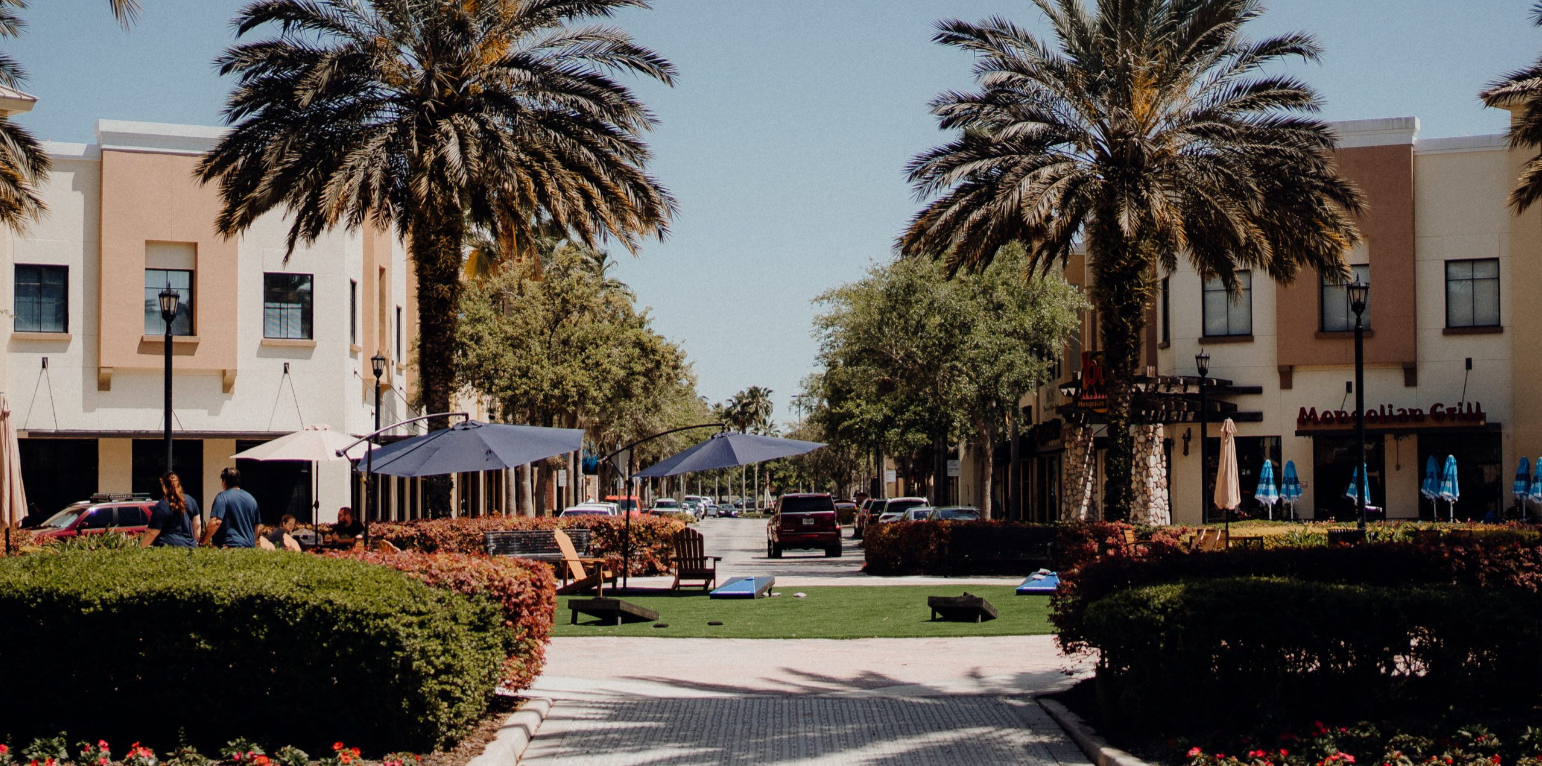 Palm-lined courtyard with beige buildings, red flowers, and a central walkway under a clear blue sky
