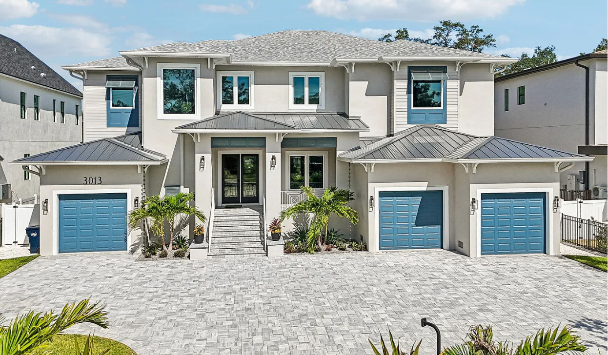 Luxury two-story white house with three blue garage doors and stone driveway