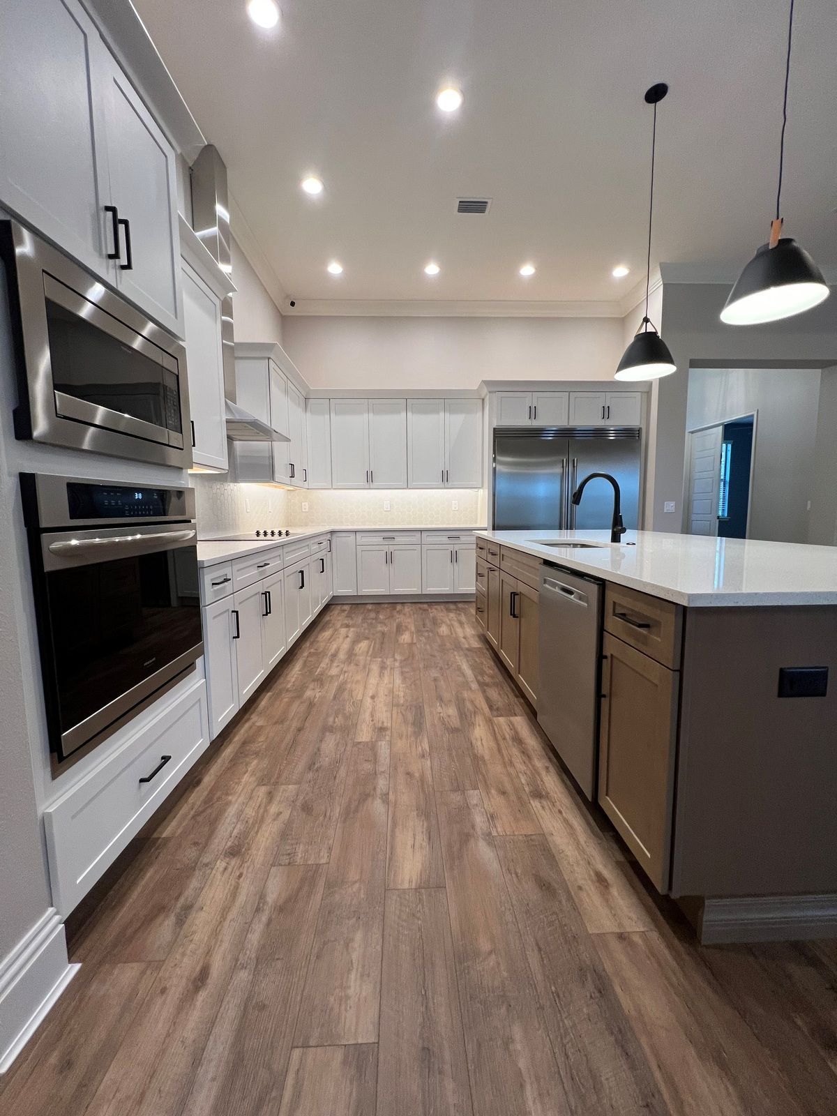 A modern kitchen featuring white cabinets, stainless steel appliances, a large center island, and wood-look flooring.