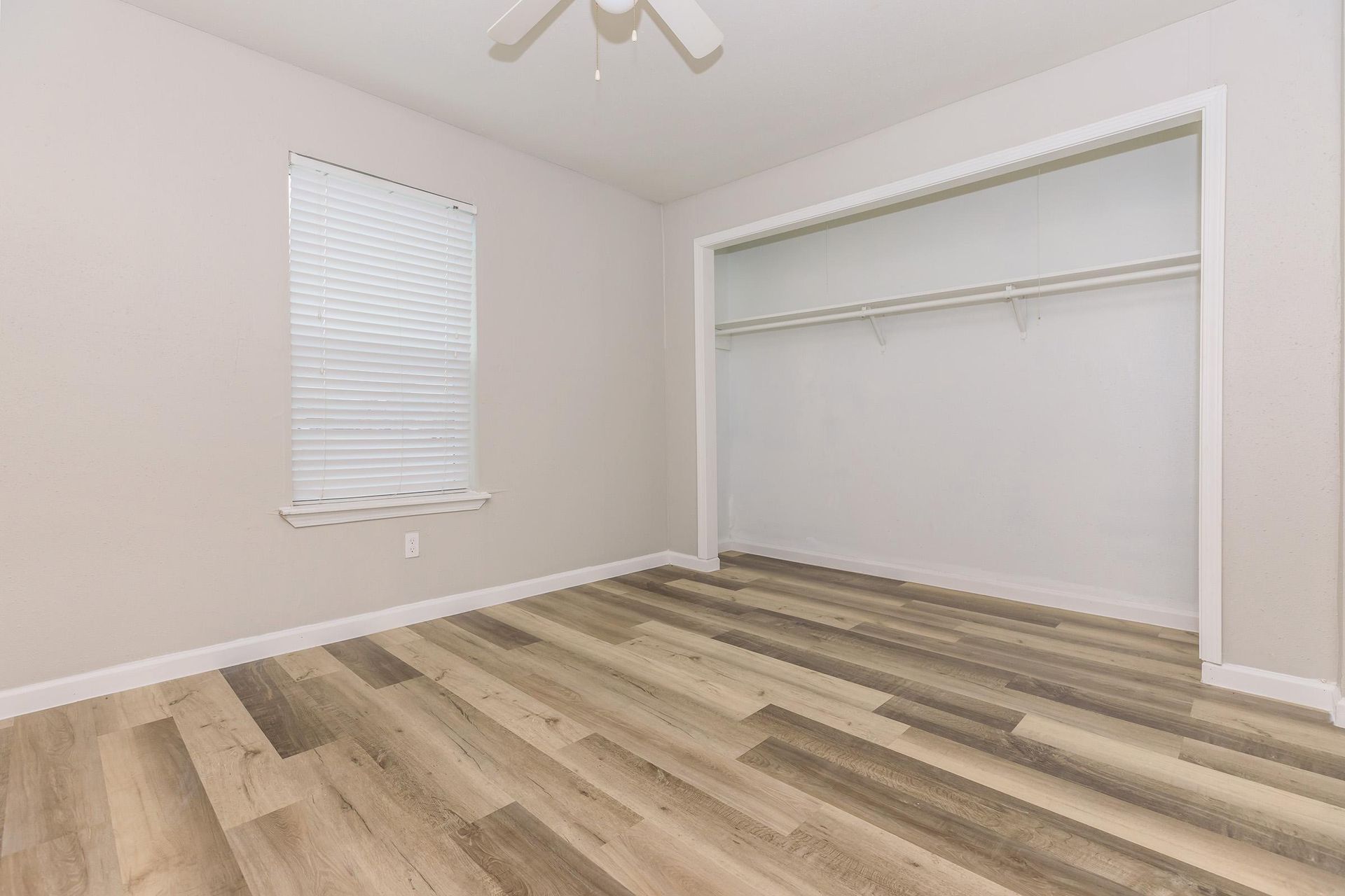 Empty bedroom with wood-look flooring, white walls, a ceiling fan, and a large open closet.