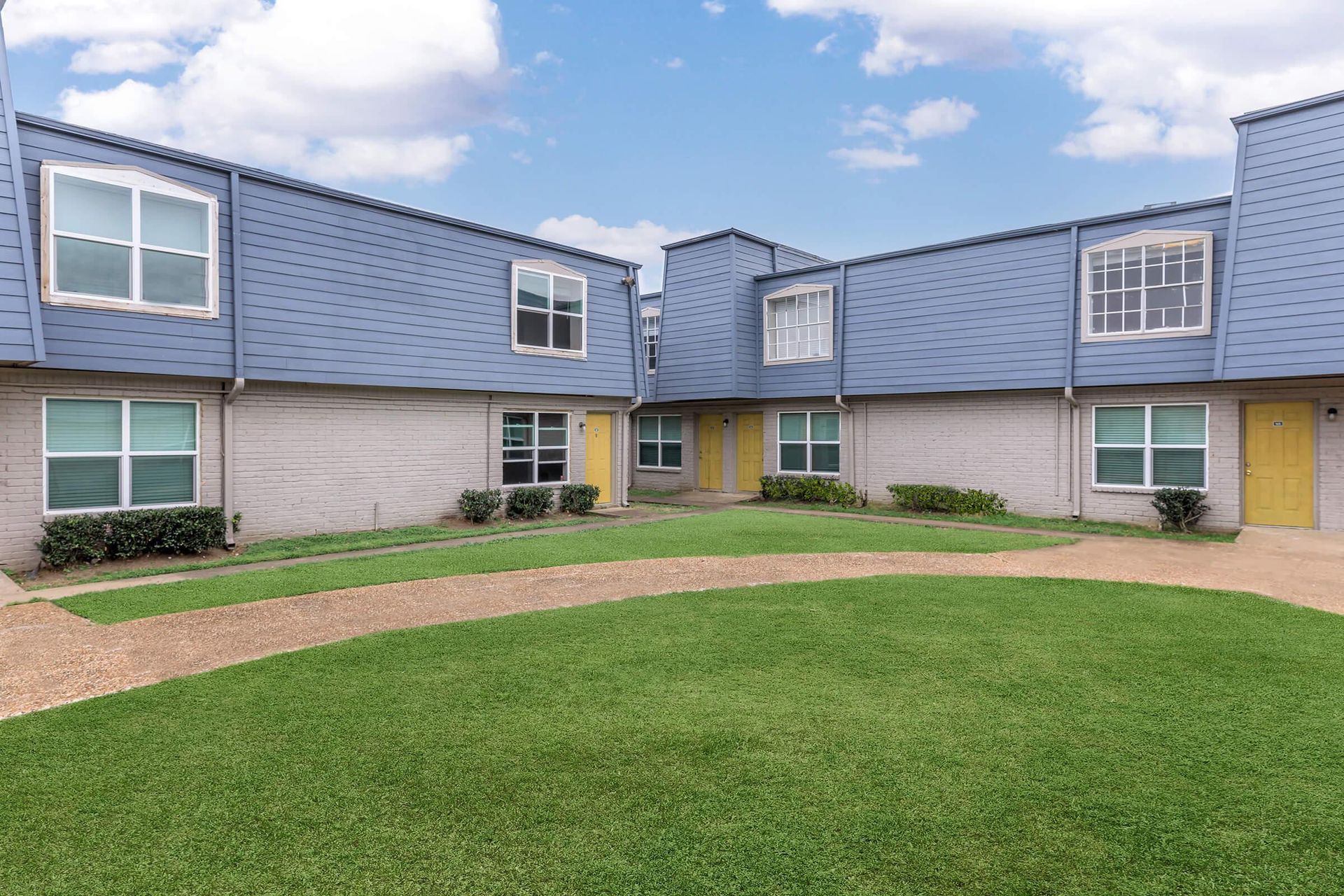 Exterior view of a multi-family apartment building courtyard with yellow doors and a grassy lawn.