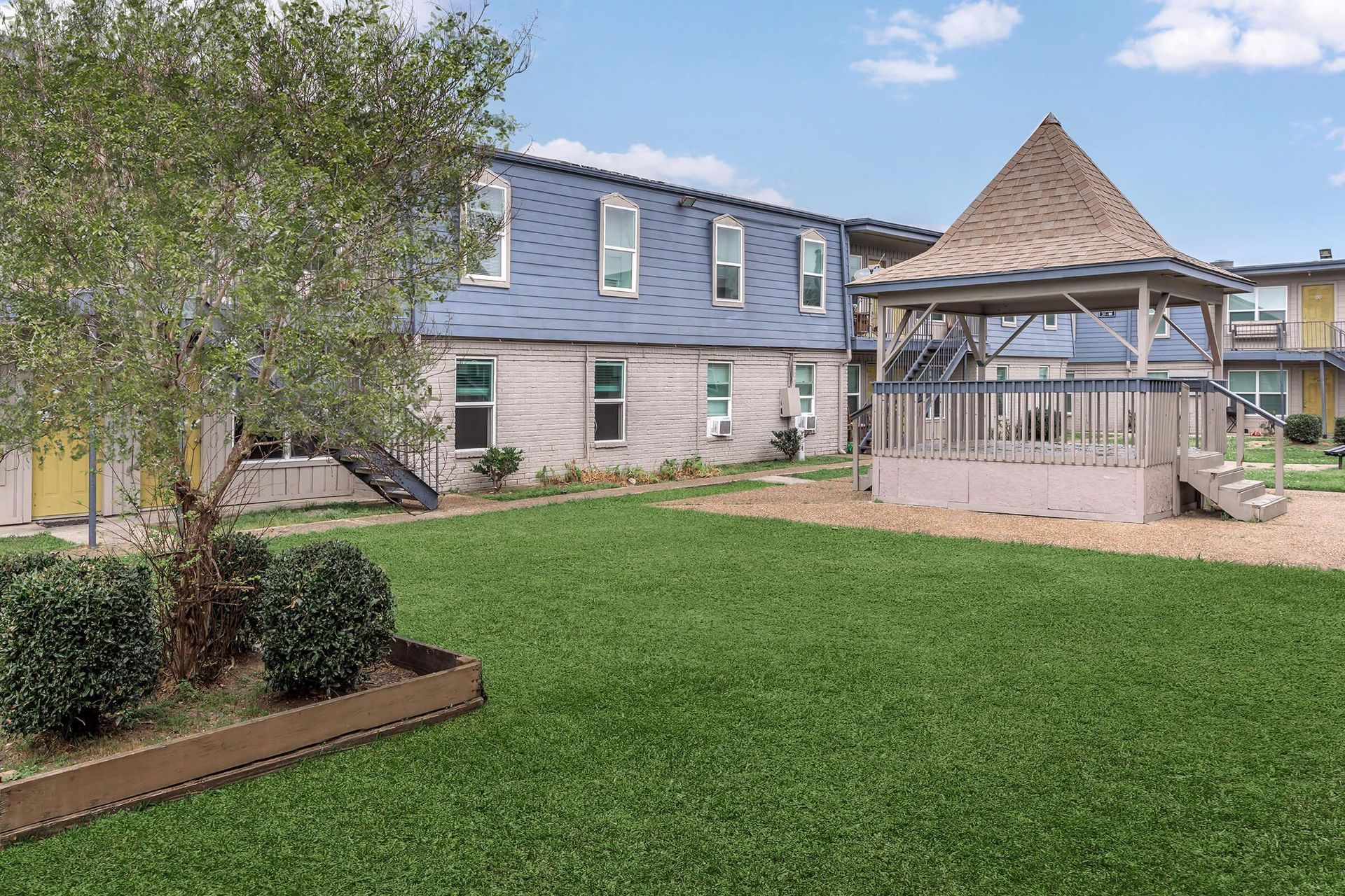 View of apartment community courtyard with gazebo, stairs, and blue siding buildings.