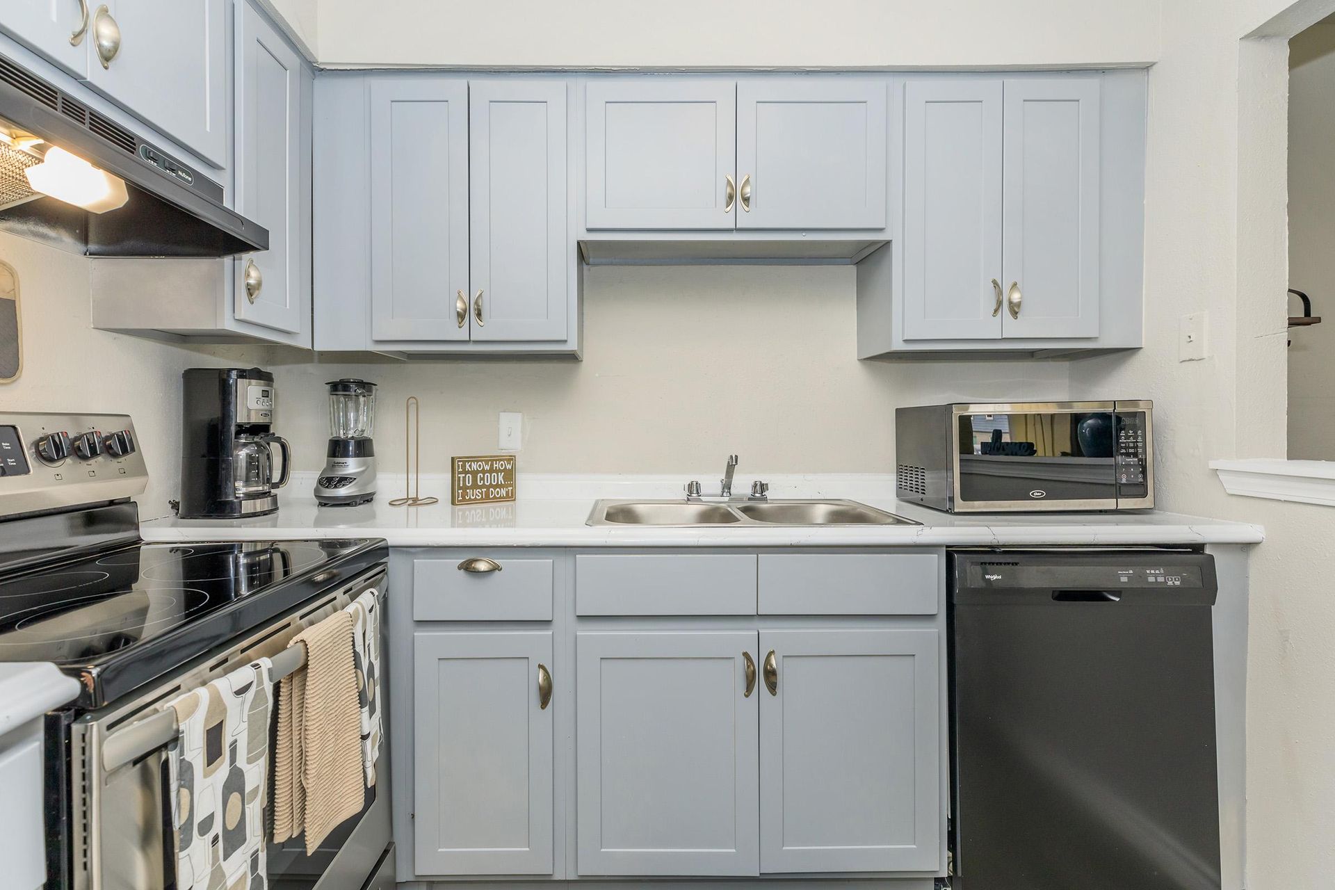 Compact kitchen with light blue cabinets, a double sink, stove, dishwasher, and a microwave.