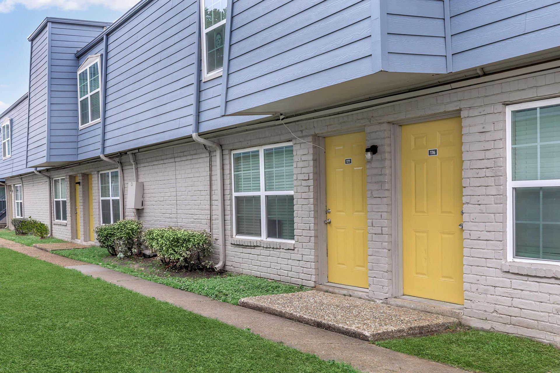Exterior view of a multi-unit apartment building with yellow doors and blue siding.