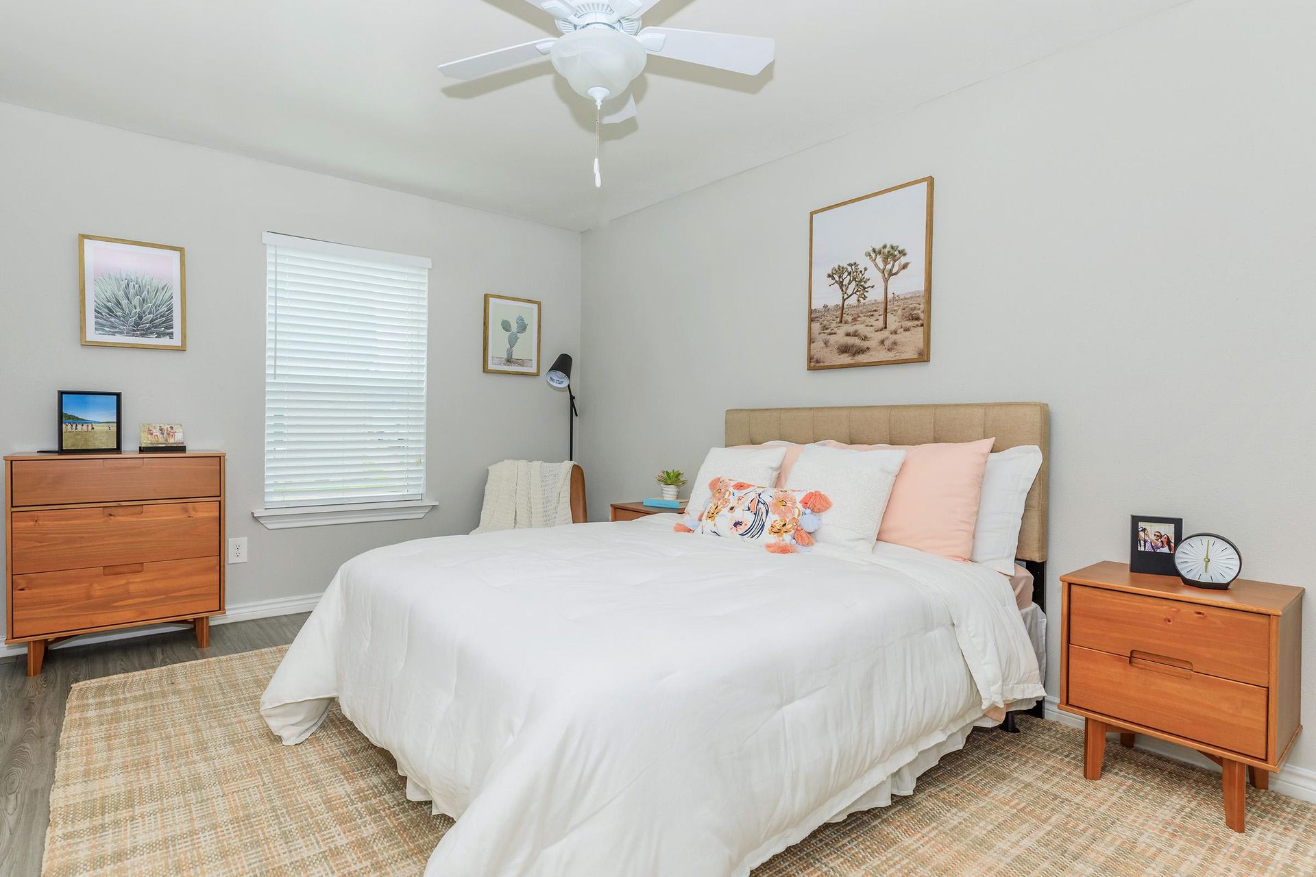 Bedroom in an apartment with a queen bed, wooden nightstands, dresser, ceiling fan, and window blinds.