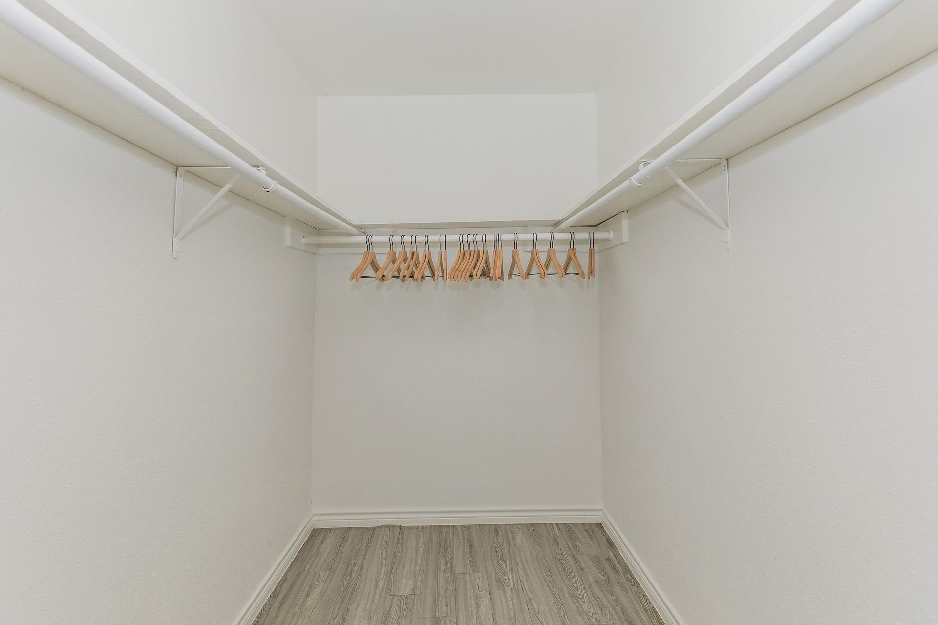 Bright walk-in closet with white walls, double hanging rods, and wooden hangers.