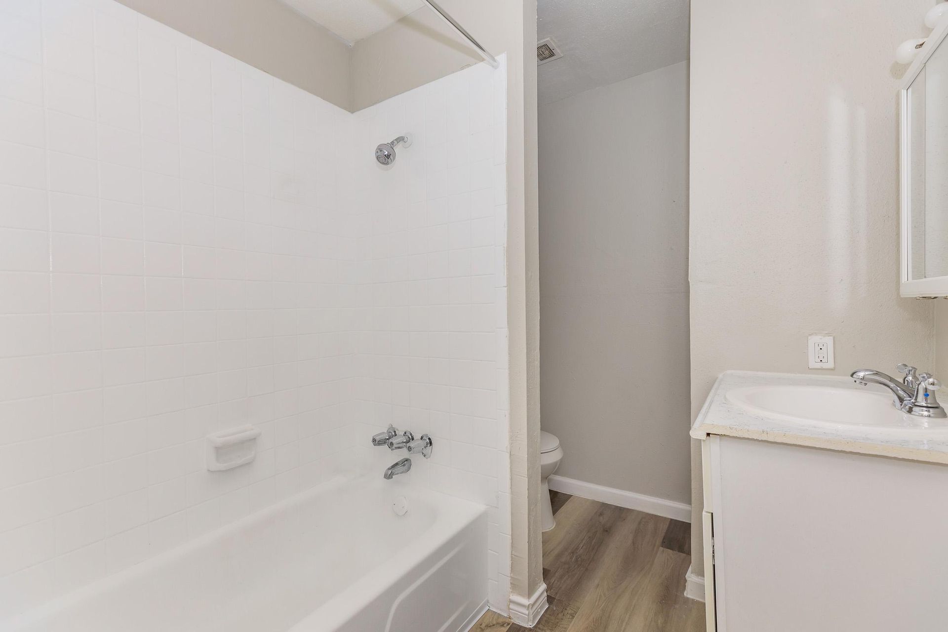 Bathroom with white tile shower/tub, toilet alcove, and vanity.