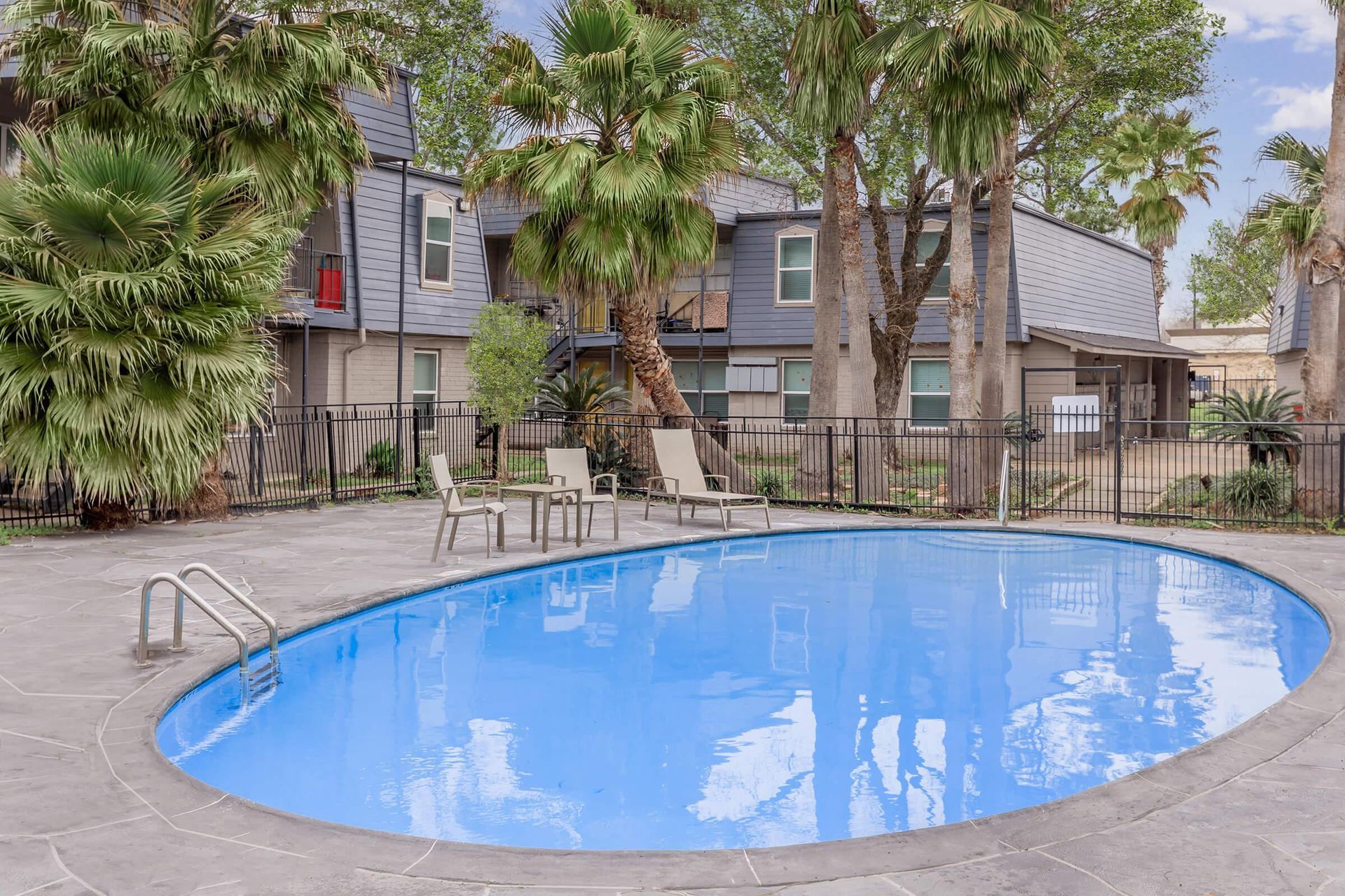 Outdoor apartment community pool with blue water, palm trees, and lounge chairs.
