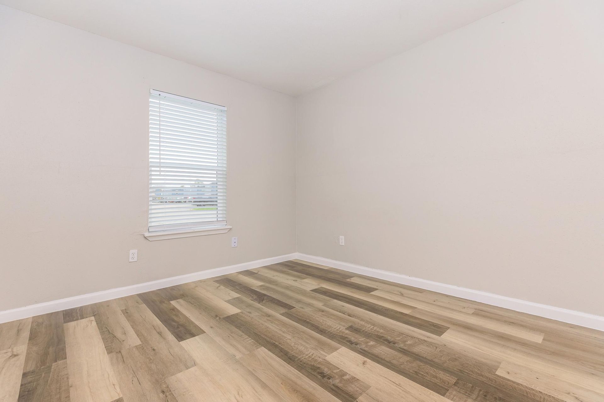 Empty beige room with a window and blinds, wood-look flooring.