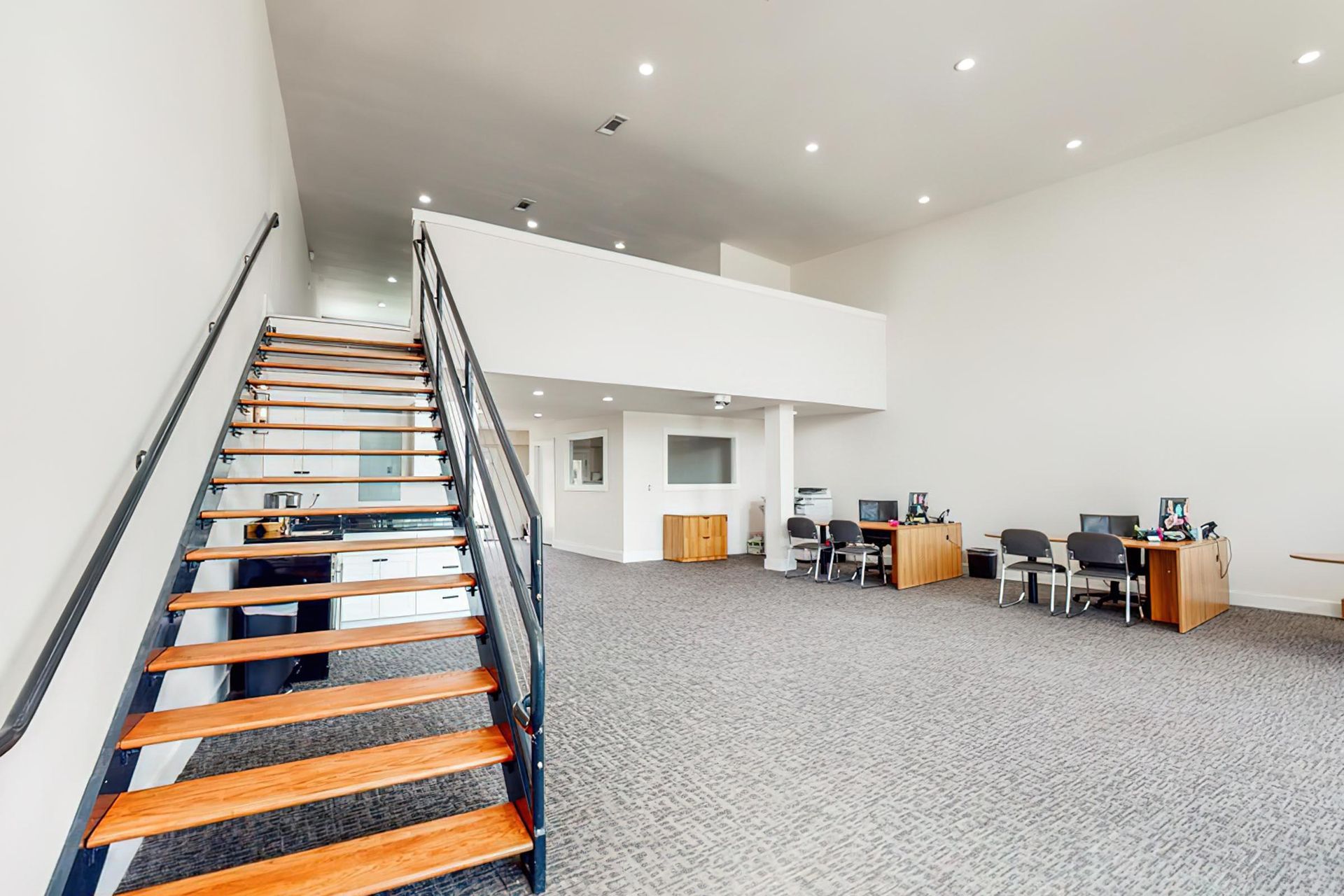 Two-story community lounge with a staircase and desks in a modern apartment complex.