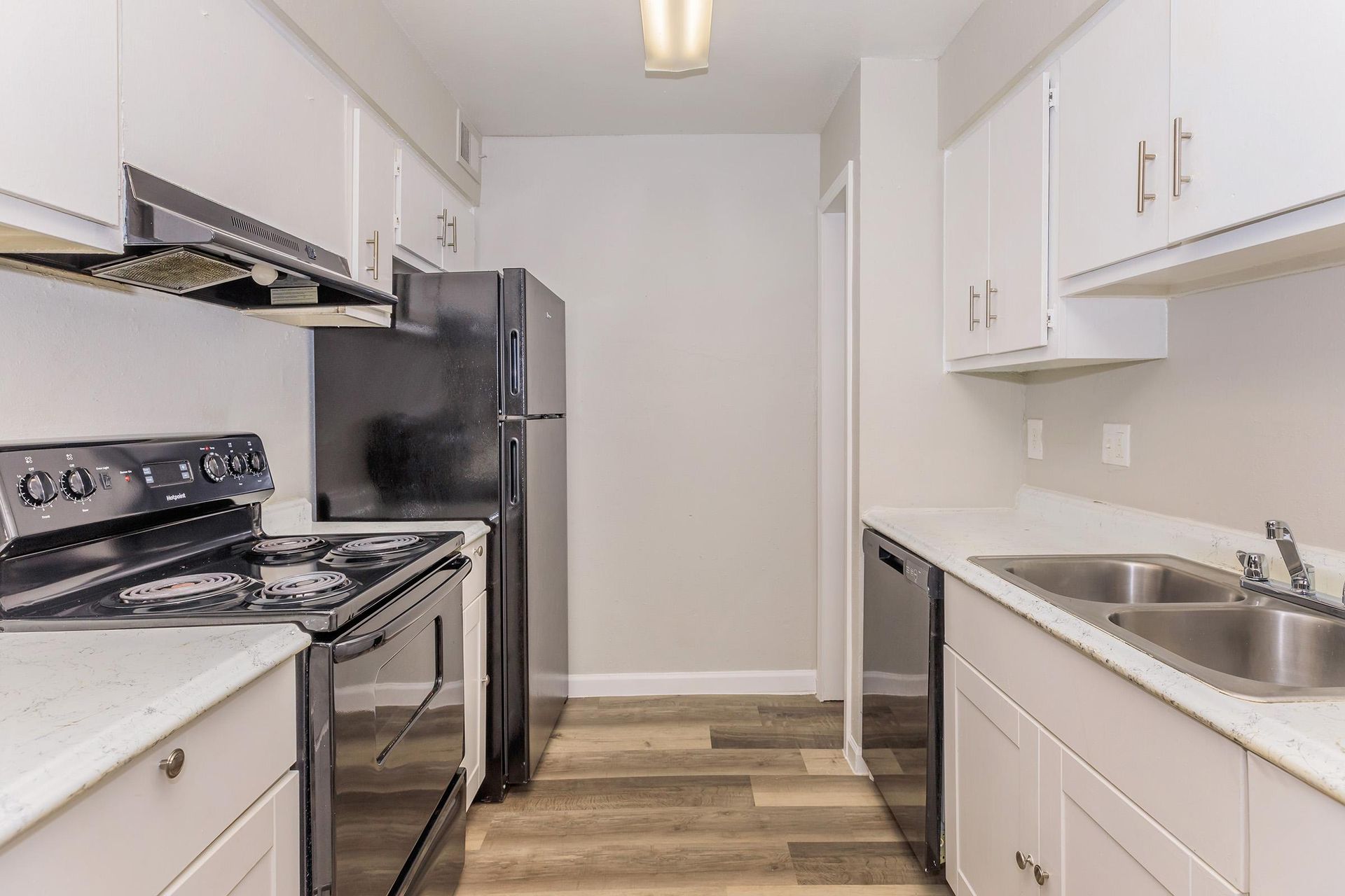 Galley kitchen with white cabinets, black appliances, and a double sink.