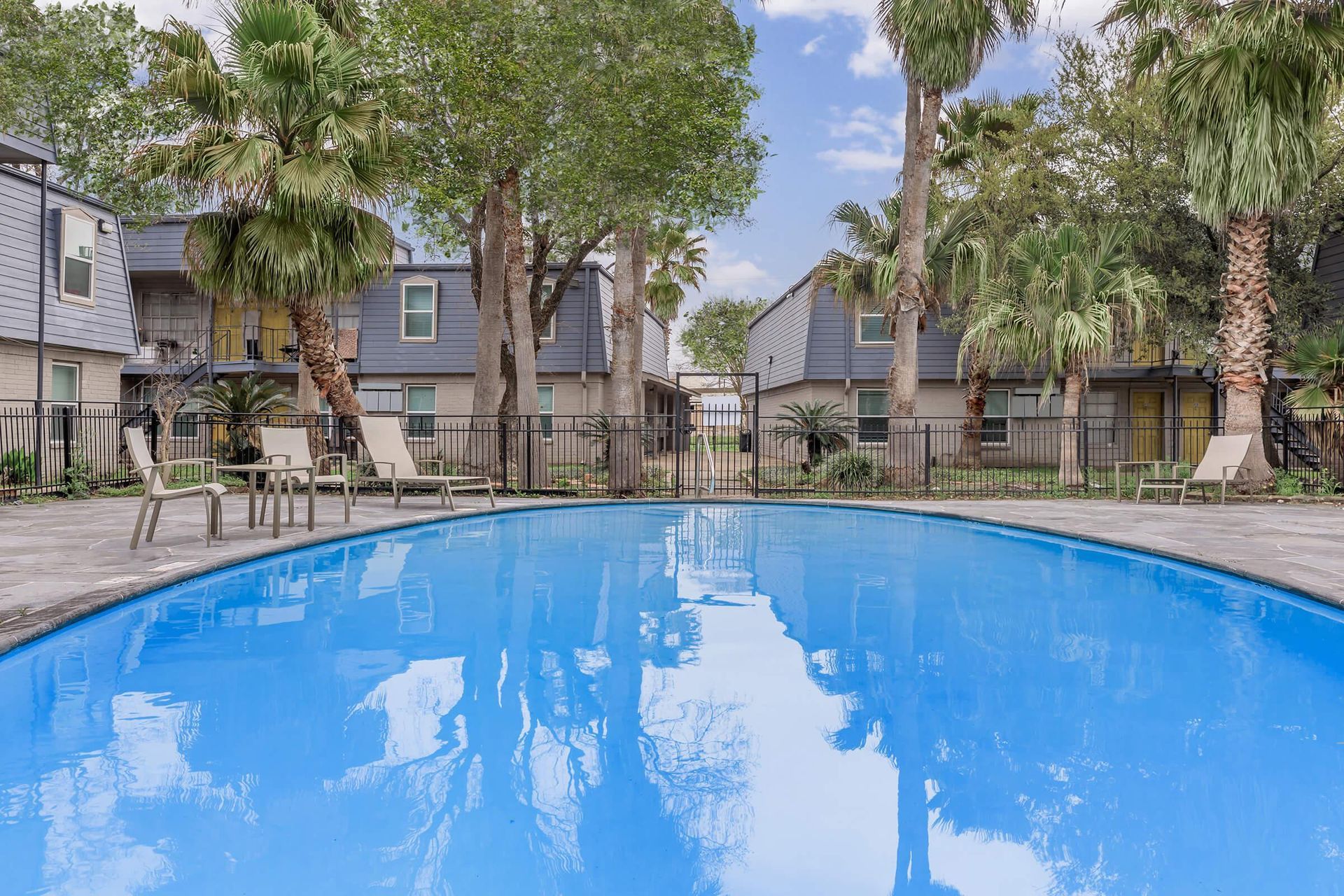 Blue outdoor pool surrounded by palm trees and lounge chairs at a multifamily complex.
