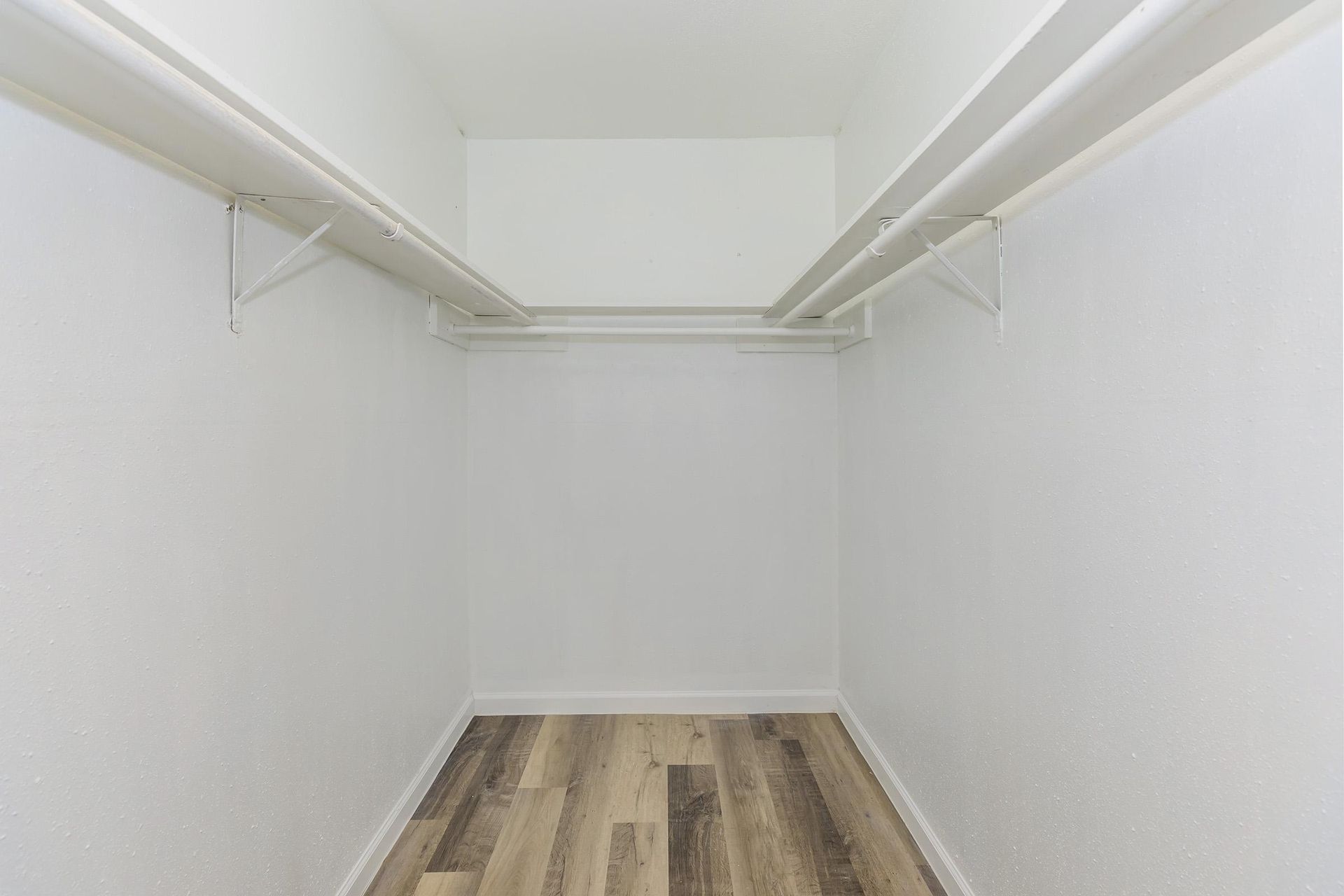 Empty walk-in closet with white walls and double hanging rods.