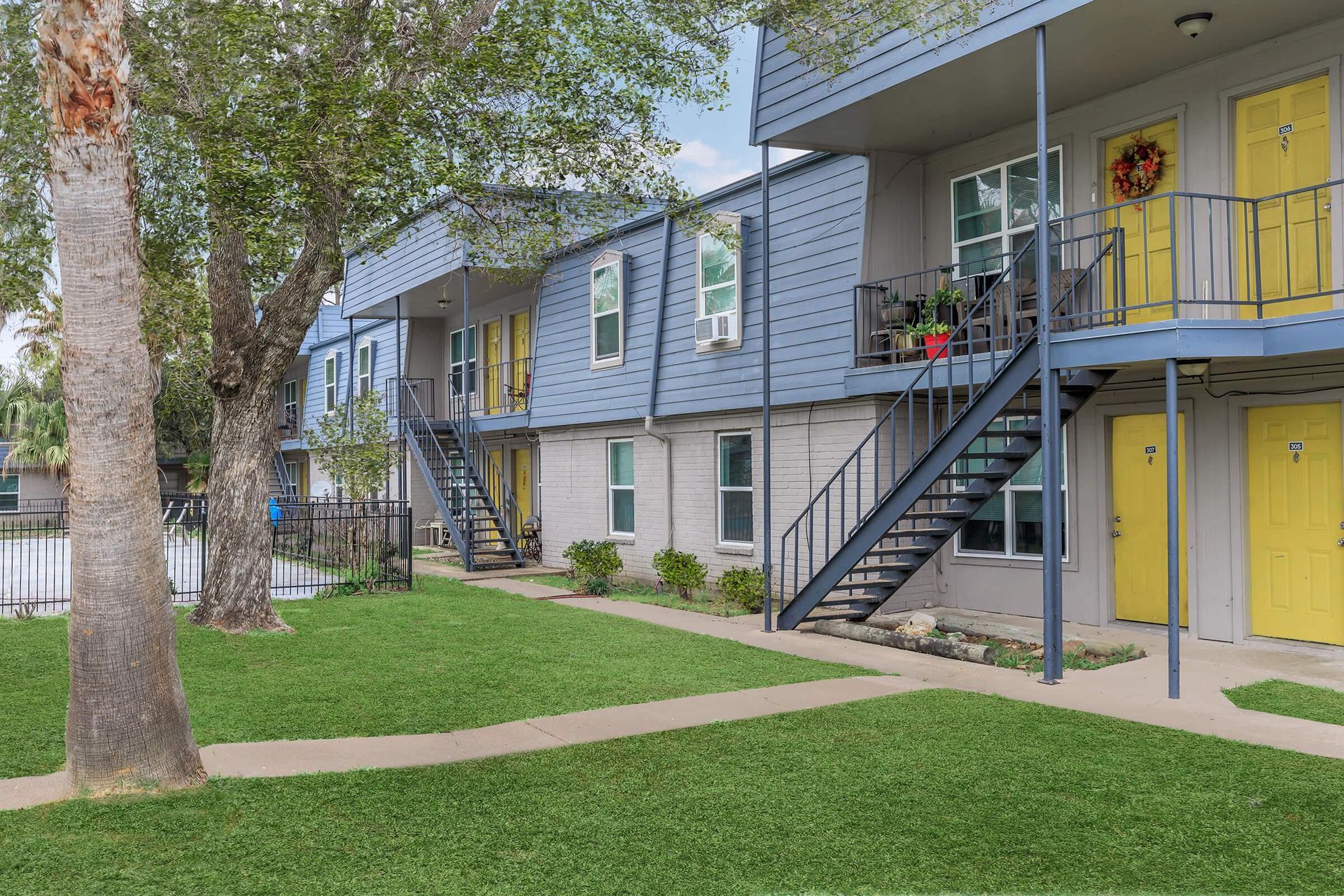 Exterior view of a multi-family building with blue siding, yellow doors, stairs, and a green lawn.