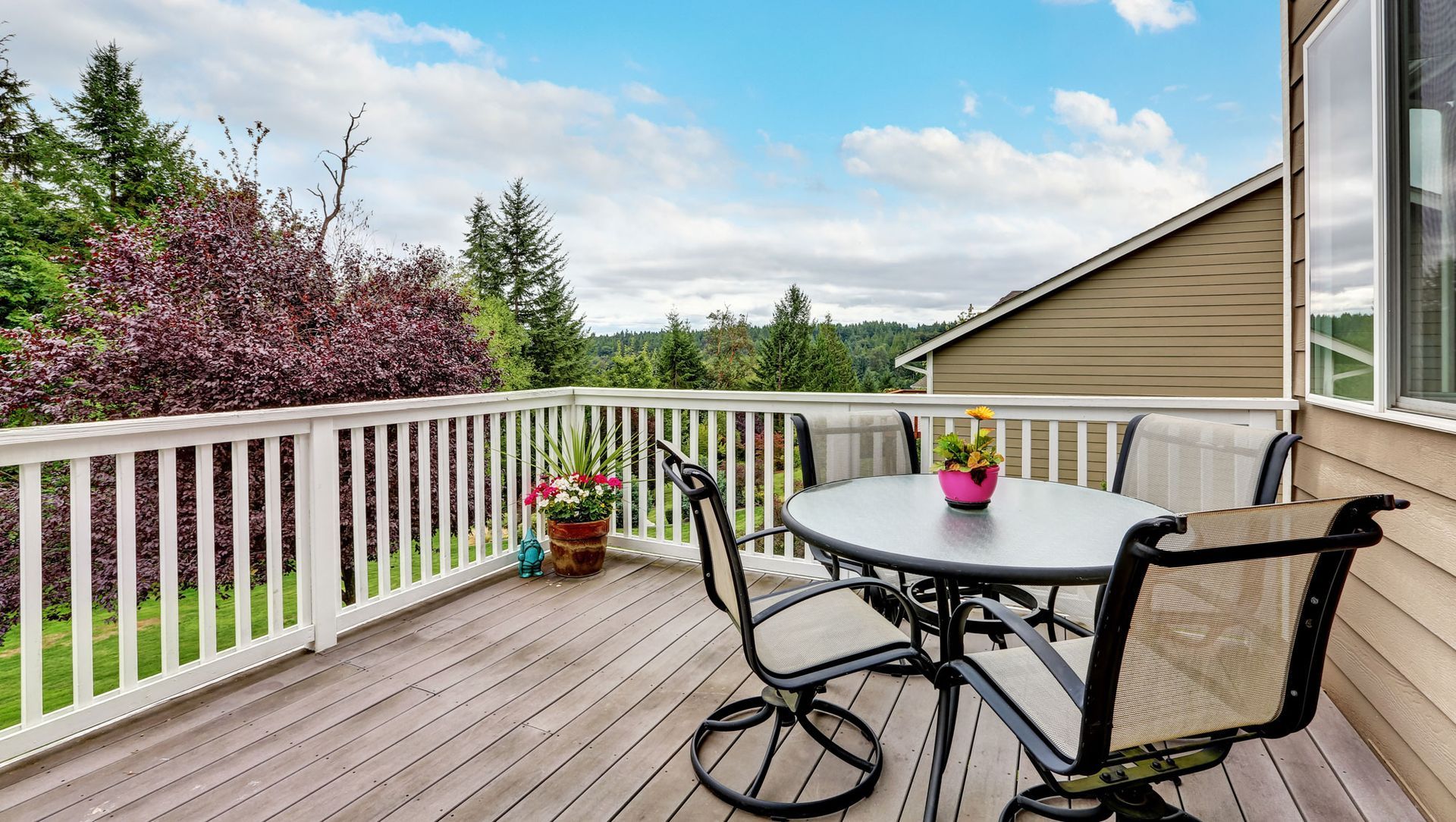 wooden walkout deck with white railings, flower pots, outdoor furniture and beautiful landscape view
