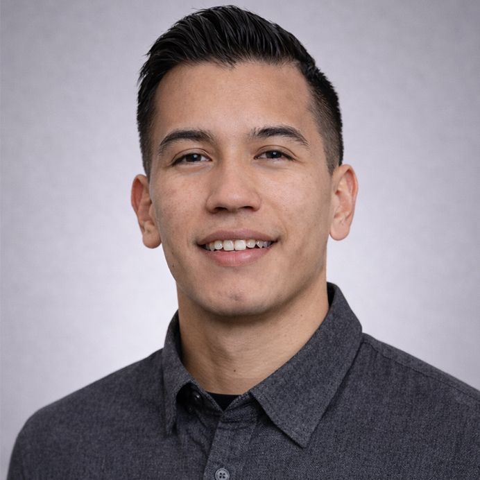 Head-and-shoulders portrait of a person with a short, dark hairstyle, centered in an orange circle with a teal border.