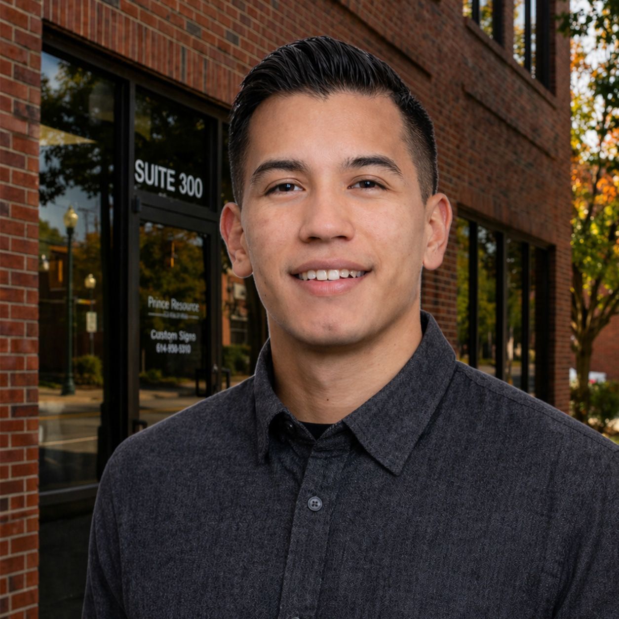 Headshot of a smiling person in a dark gray button-up shirt against a light gray background