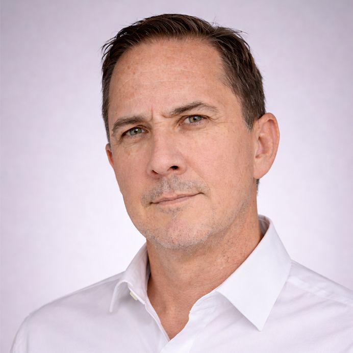 A person with short dark hair in a white shirt, looking off-camera against a circular orange background.