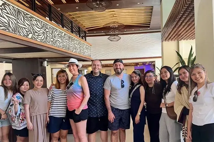 A group of ten people stands smiling in a hotel lobby with high, decorative wood ceilings and architectural lighting.