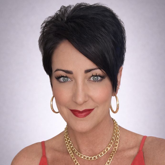 A person with short, dark hair wears a red top, gold hoop earrings, and a layered gold chain necklace against an orange background.