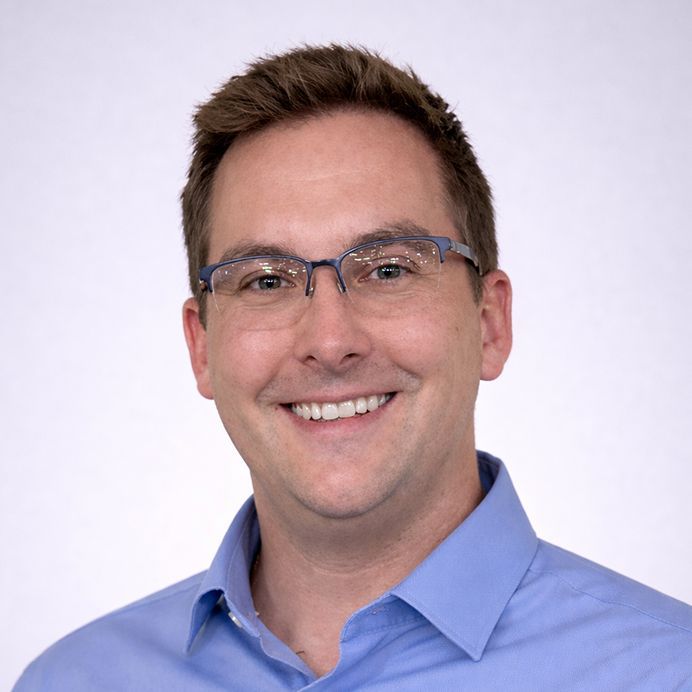 A person with short hair and glasses smiling in a circular frame with an orange background and teal border.