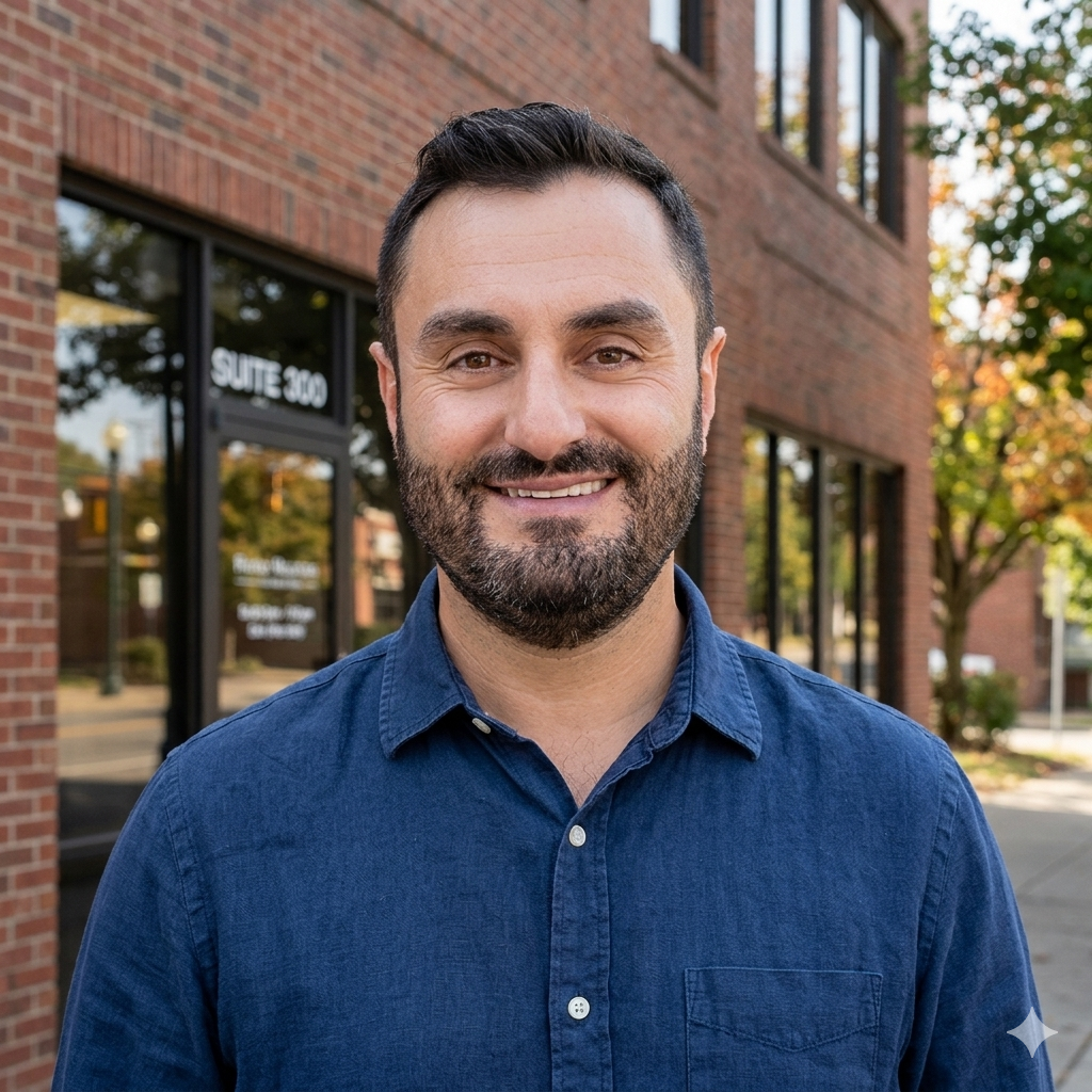 Smiling bearded man in a light patterned shirt against a gray background