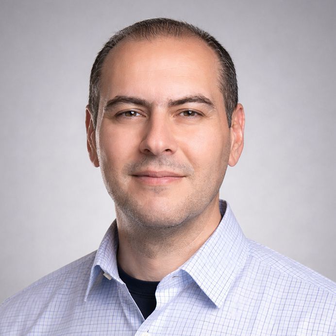 A headshot of a person with short hair wearing a plaid shirt, framed in a circle with an orange background and teal border.