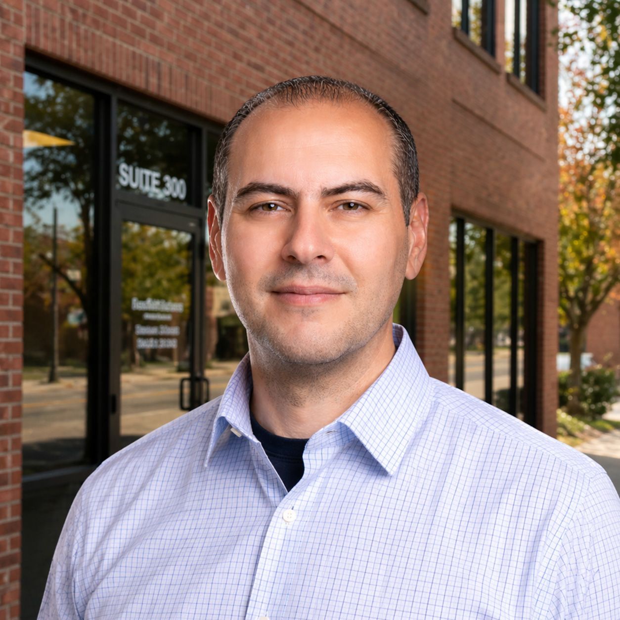 Studio headshot of a man in a light blue shirt against a gray background