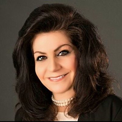 Studio portrait of a smiling woman with dark hair and a pearl necklace on a gray background