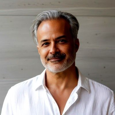 Smiling man with gray hair and beard in a white shirt against a plain light background