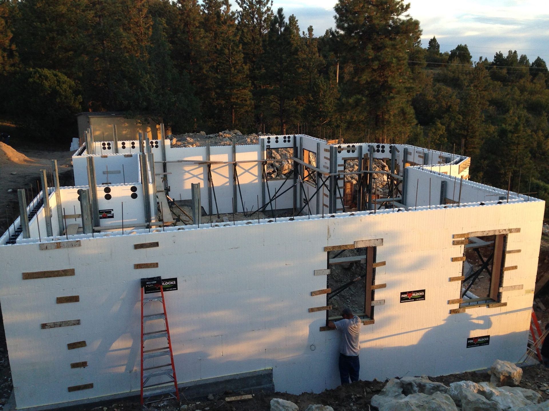 House under construction, white walls, wooden supports, worker installing a window.