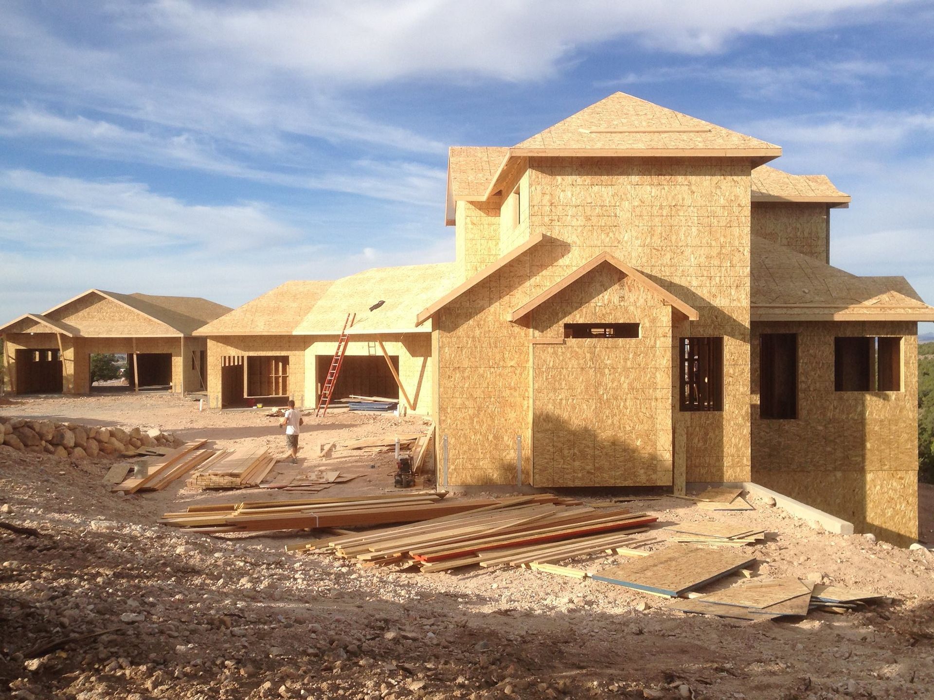 House under construction, wooden frame, on a hillside, blue sky.