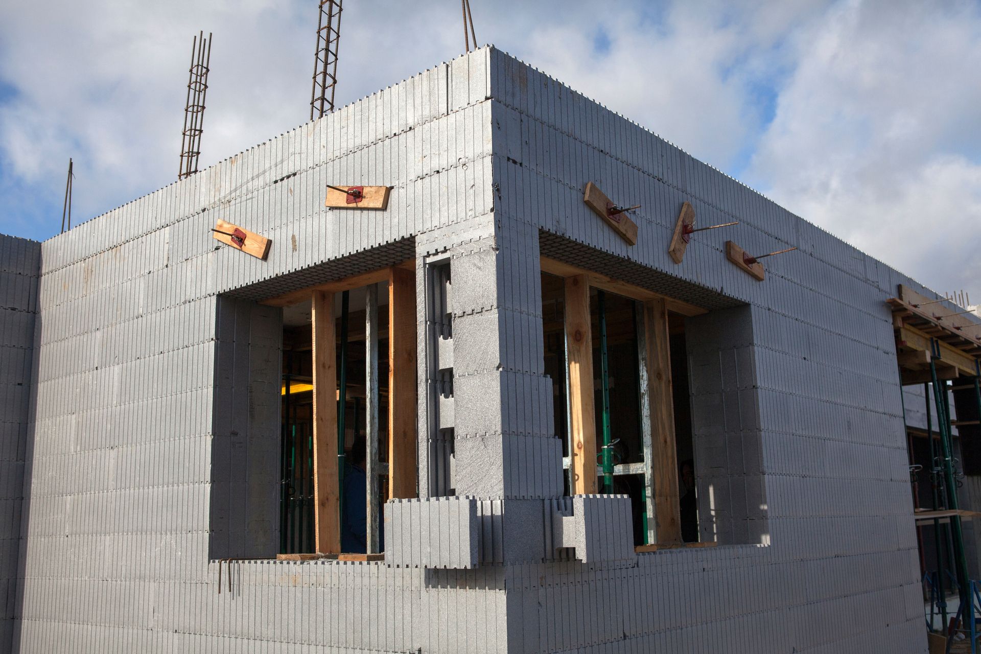Construction of a building with grey concrete blocks, wooden window frames, and blue sky background.