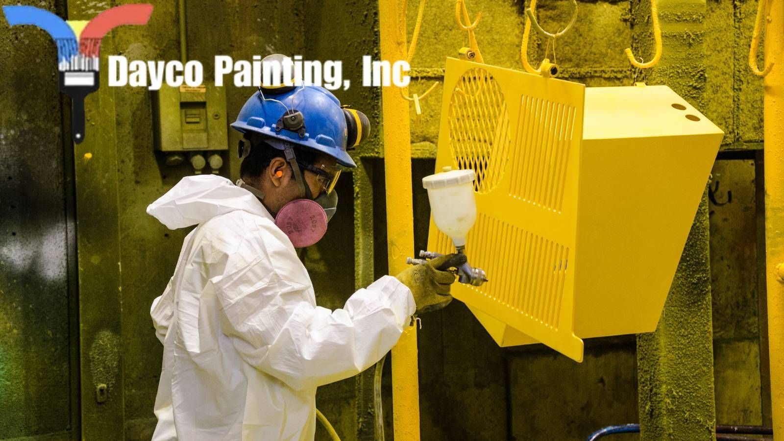 A hired painter wearing a hard hat is spray painting a yellow wall .