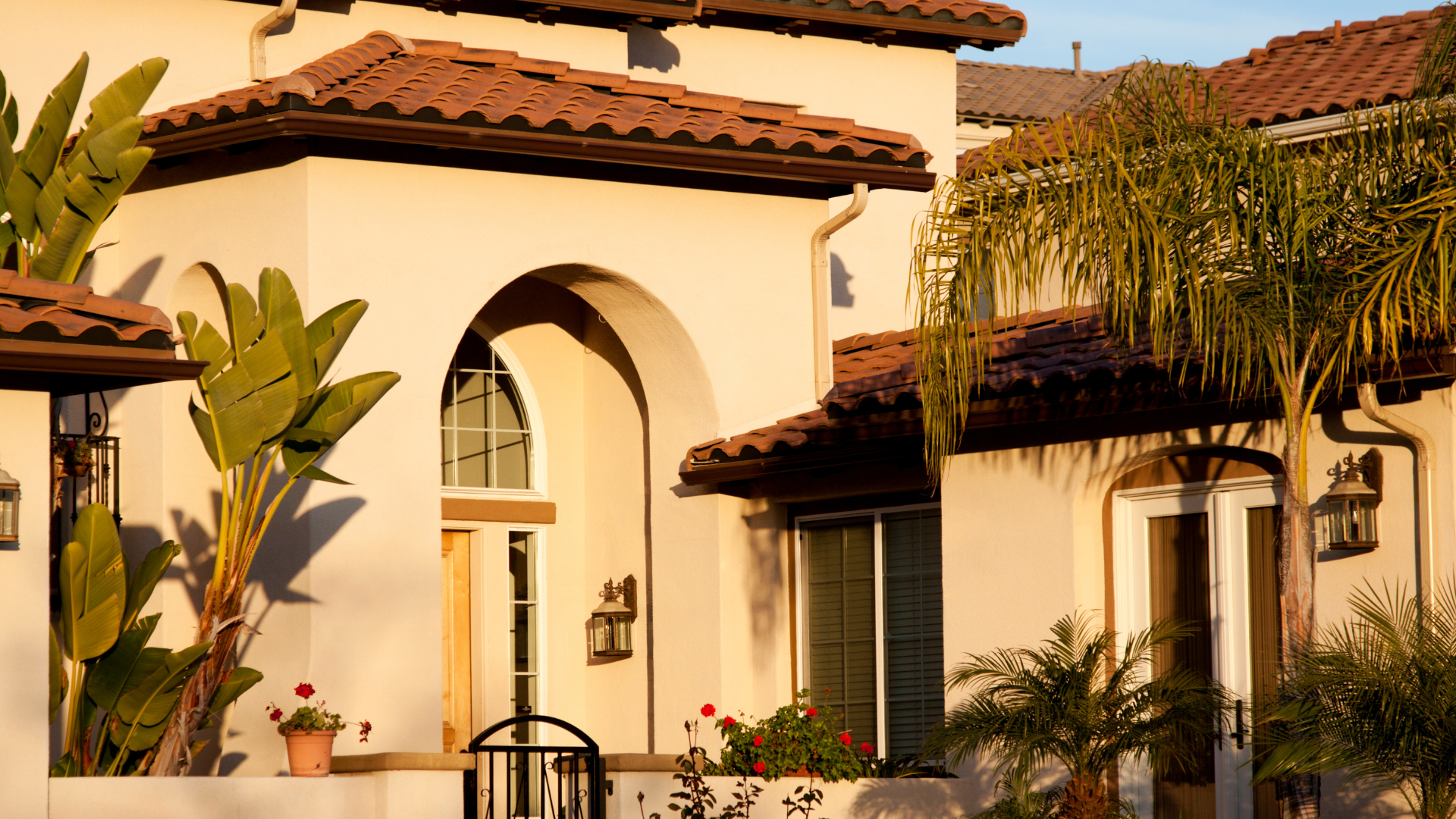 Side view of a building with brown-framed windows and a wooden walkway, lush green plants to the left.