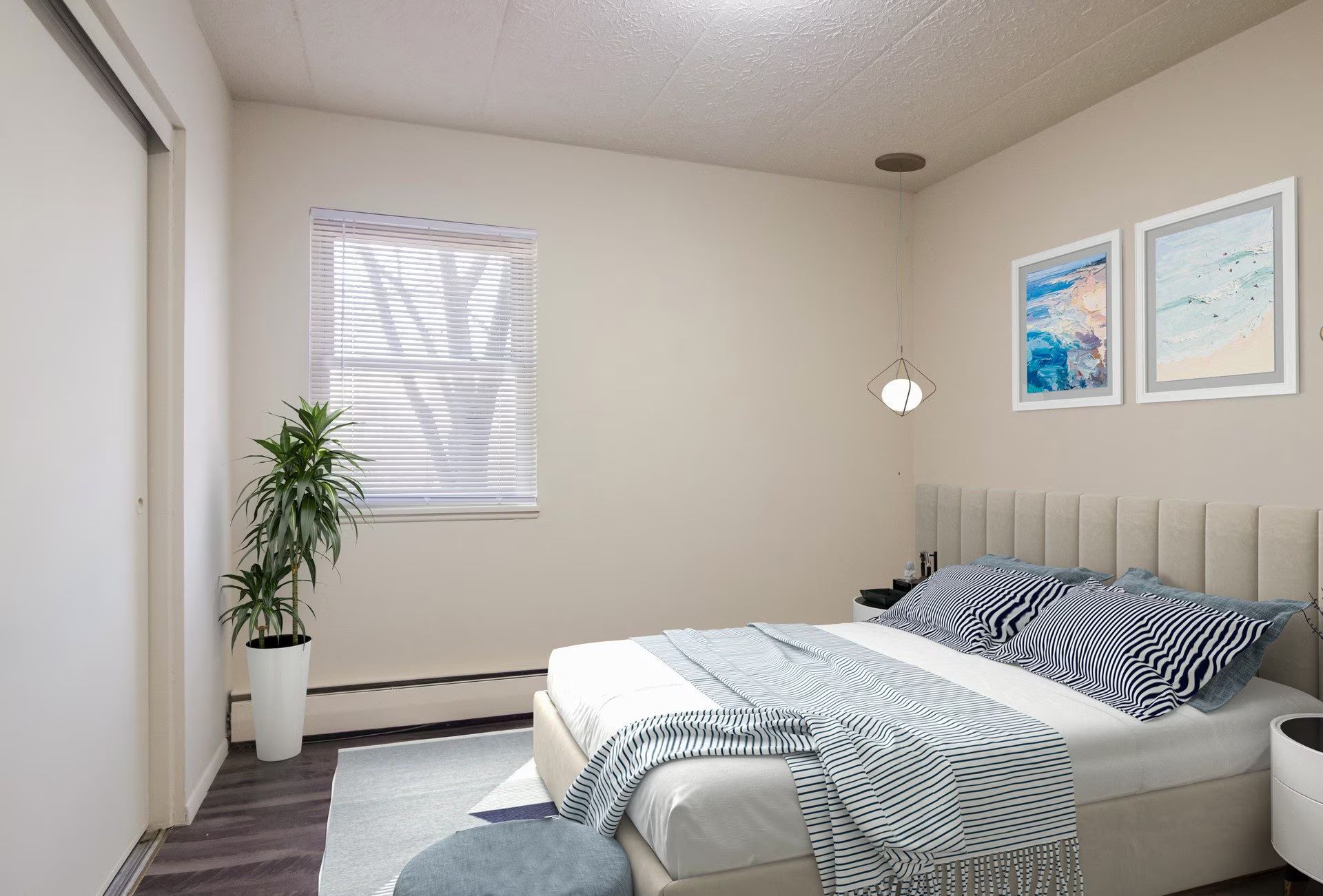 Bedroom with a bed, two framed pictures, a window, a plant, and a round ottoman on a rug.