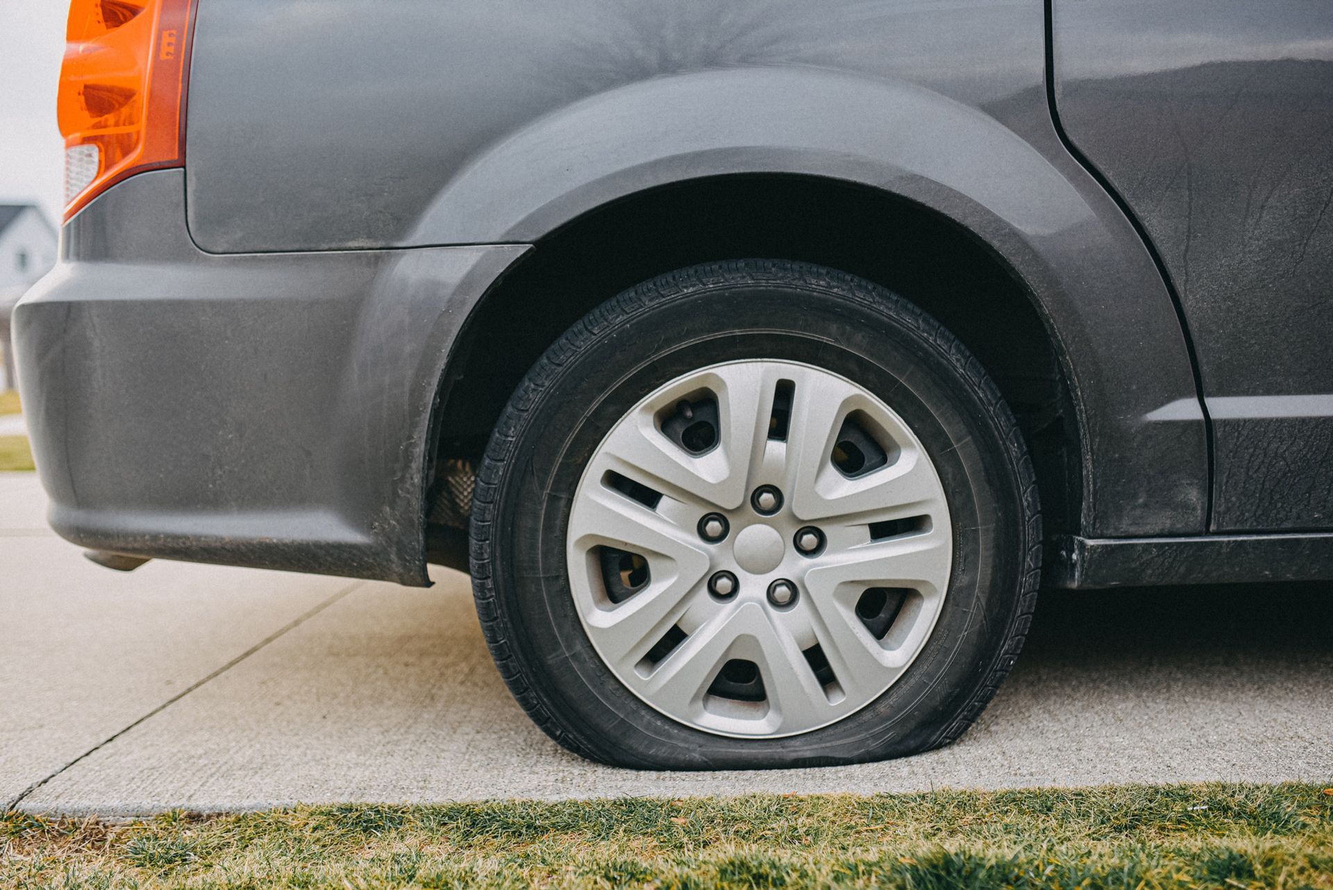Gray minivan with a flat tire on a concrete driveway next to some grass.