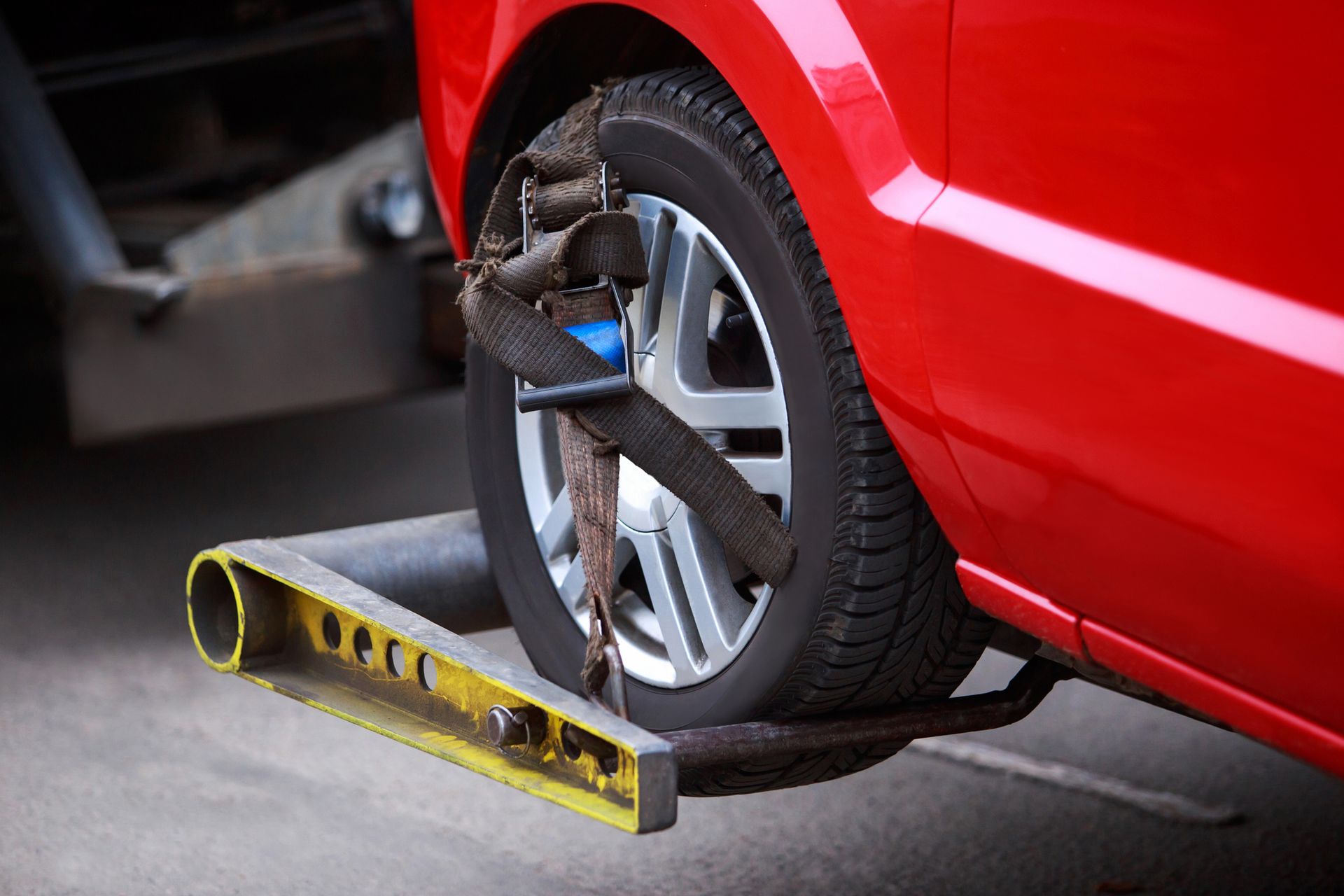 Red car wheel secured on a tow truck's platform, strapped with a black and blue belt.