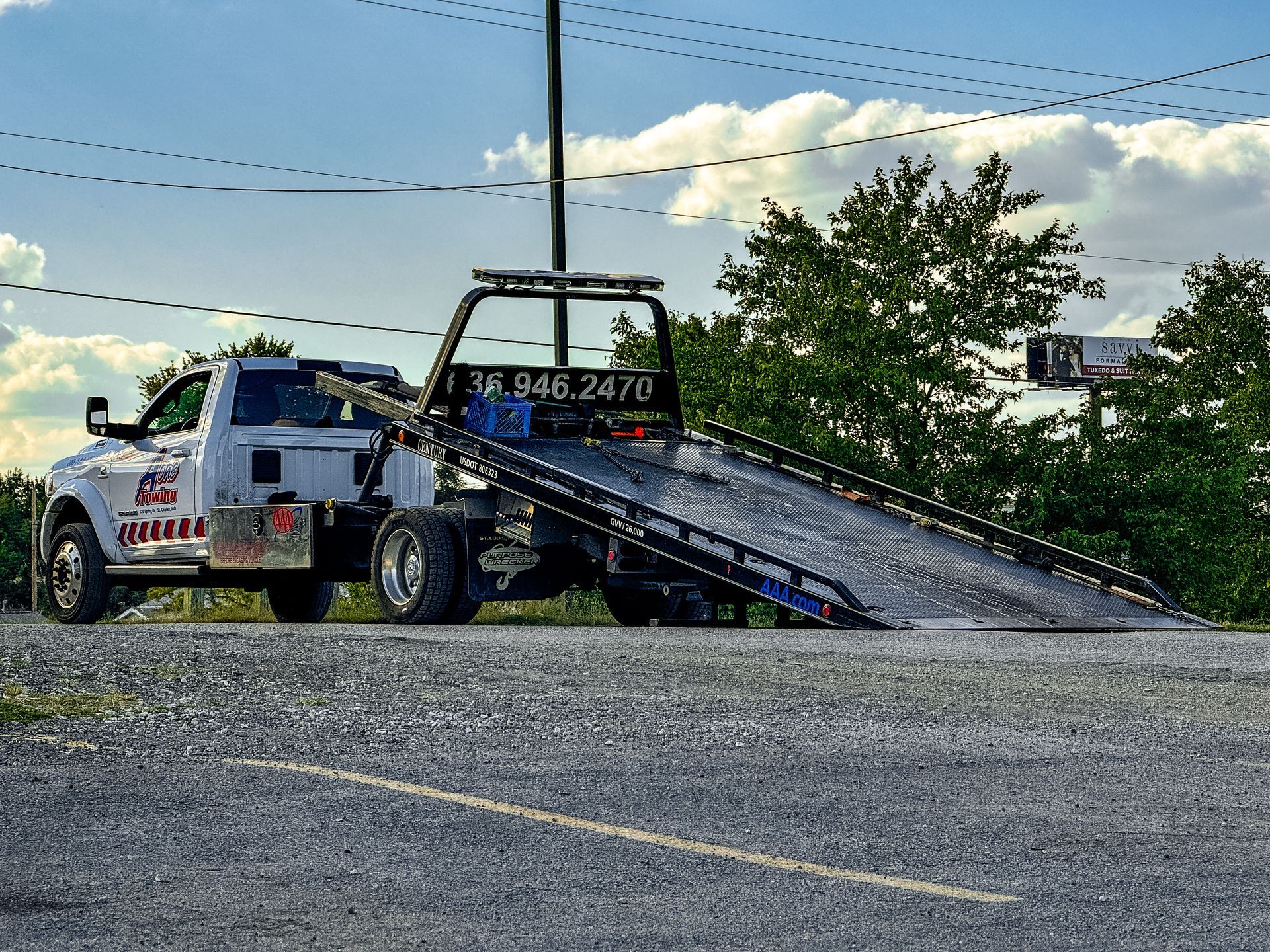 Silver car being towed on a flatbed tow truck; green trees in background.