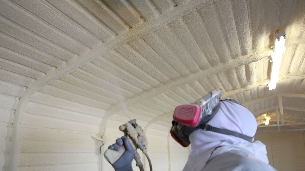 A person is spraying foam on the ceiling of a building.