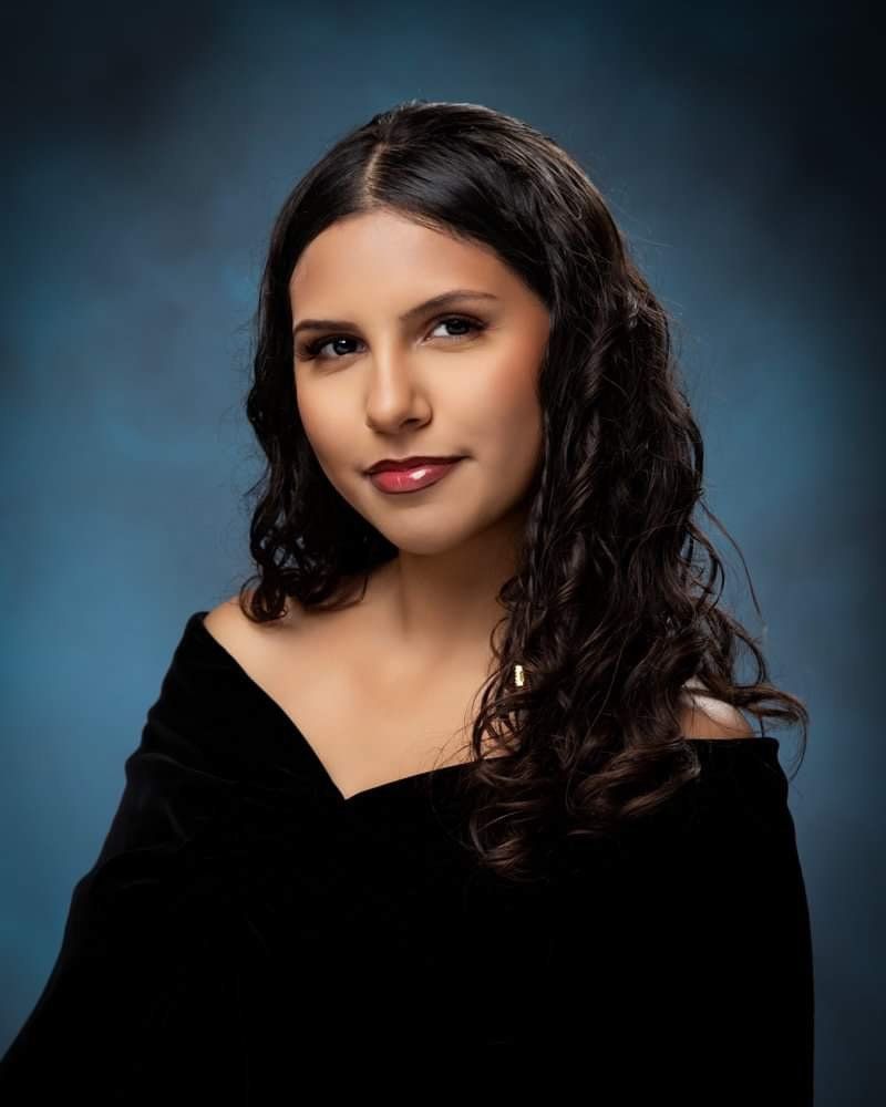 A woman with long curly hair is wearing a black off the shoulder top.