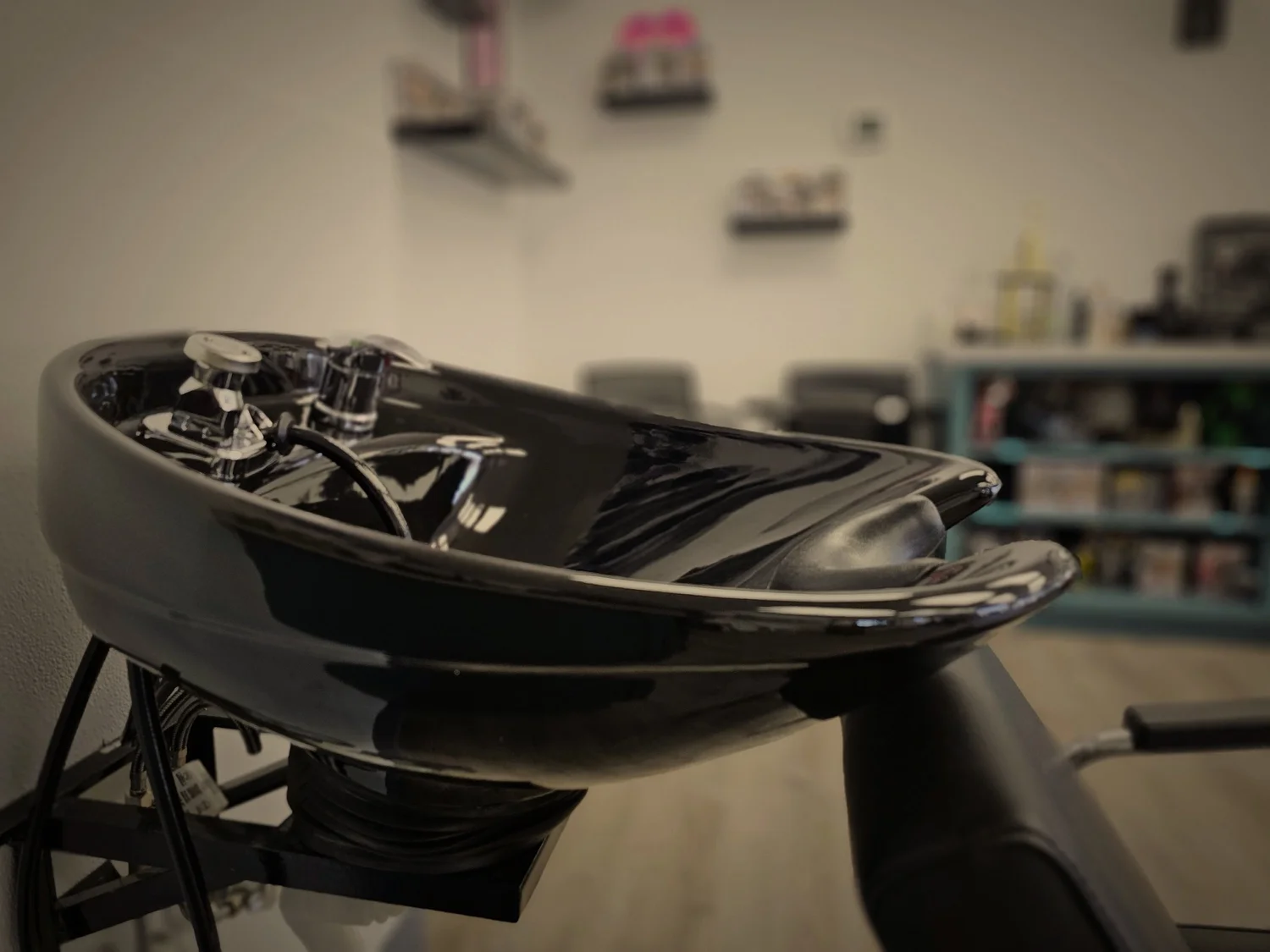 Black salon shampoo bowl, chrome fixtures, blurry background.
